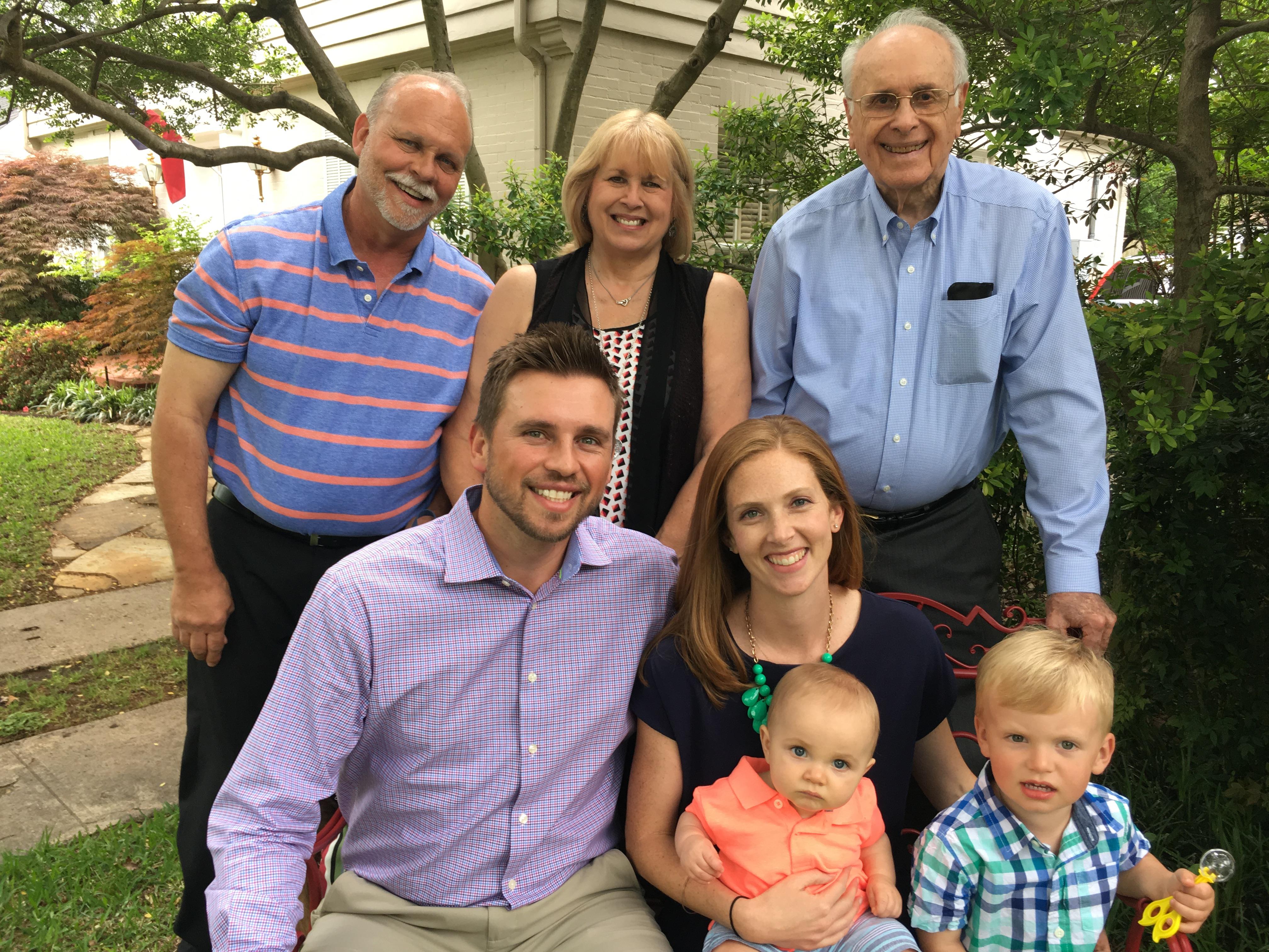Family members are enjoying a joyful moment in a garden, smiling and posing together.