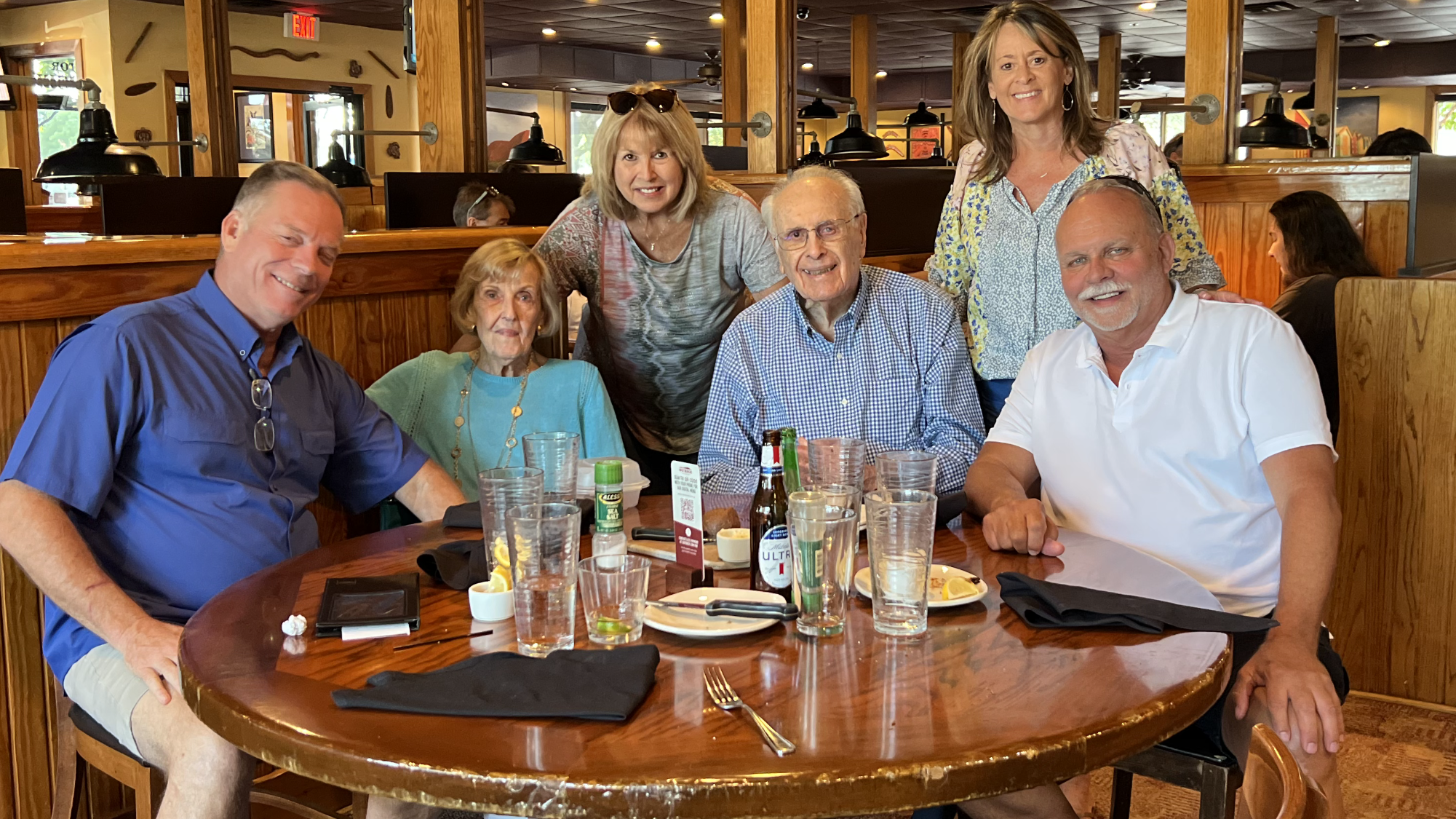 A family of six shares smiles and conversations at a restaurant table.