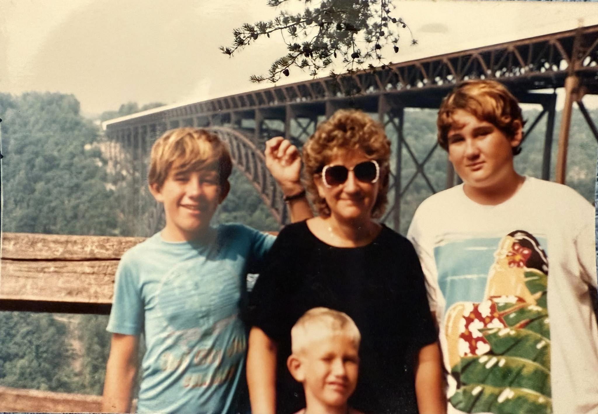 Three children and an adult woman pose together smiling with a large bridge in the background.