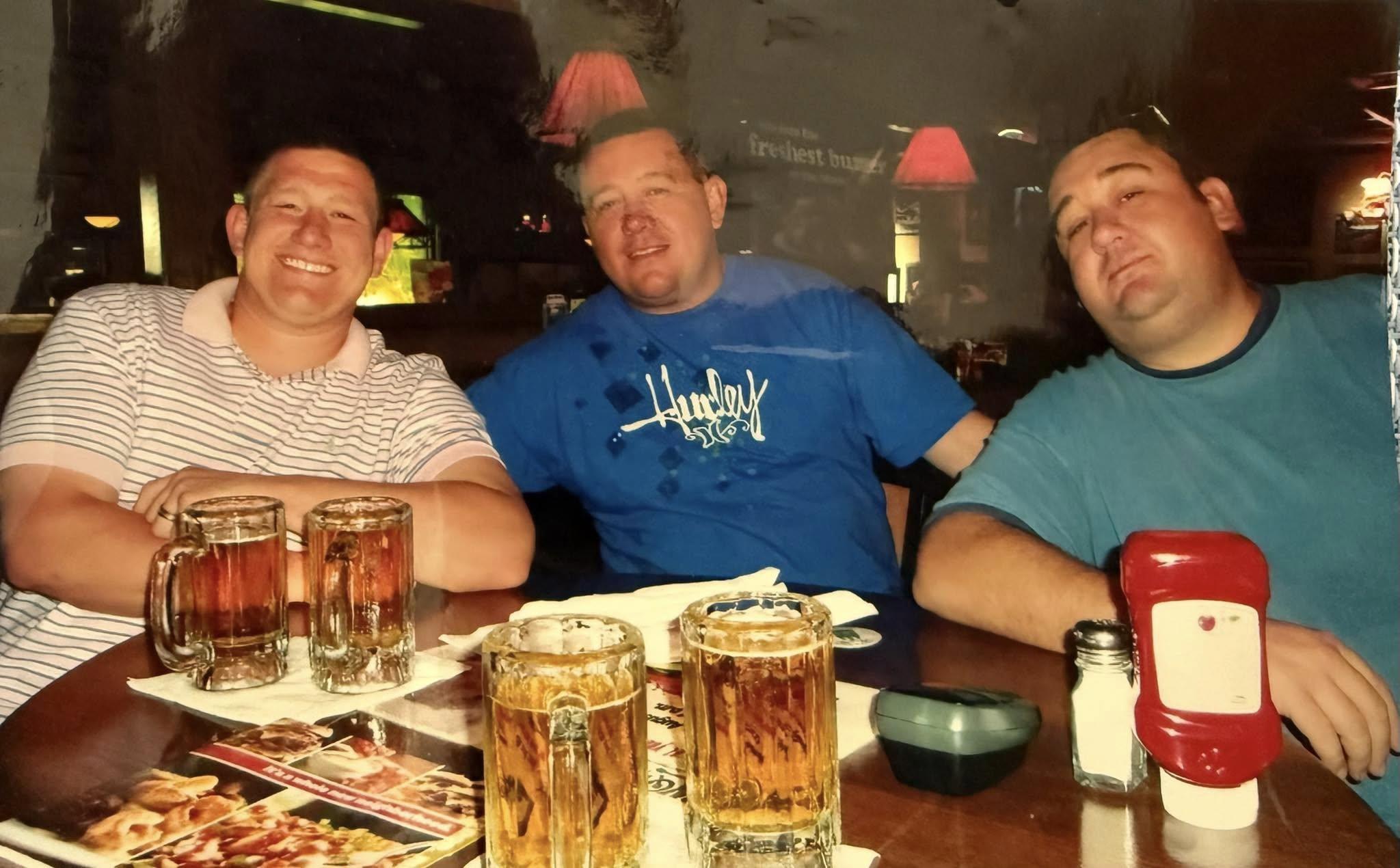 Three friends share laughs and drinks at a bar, enjoying each other's company and good food.
