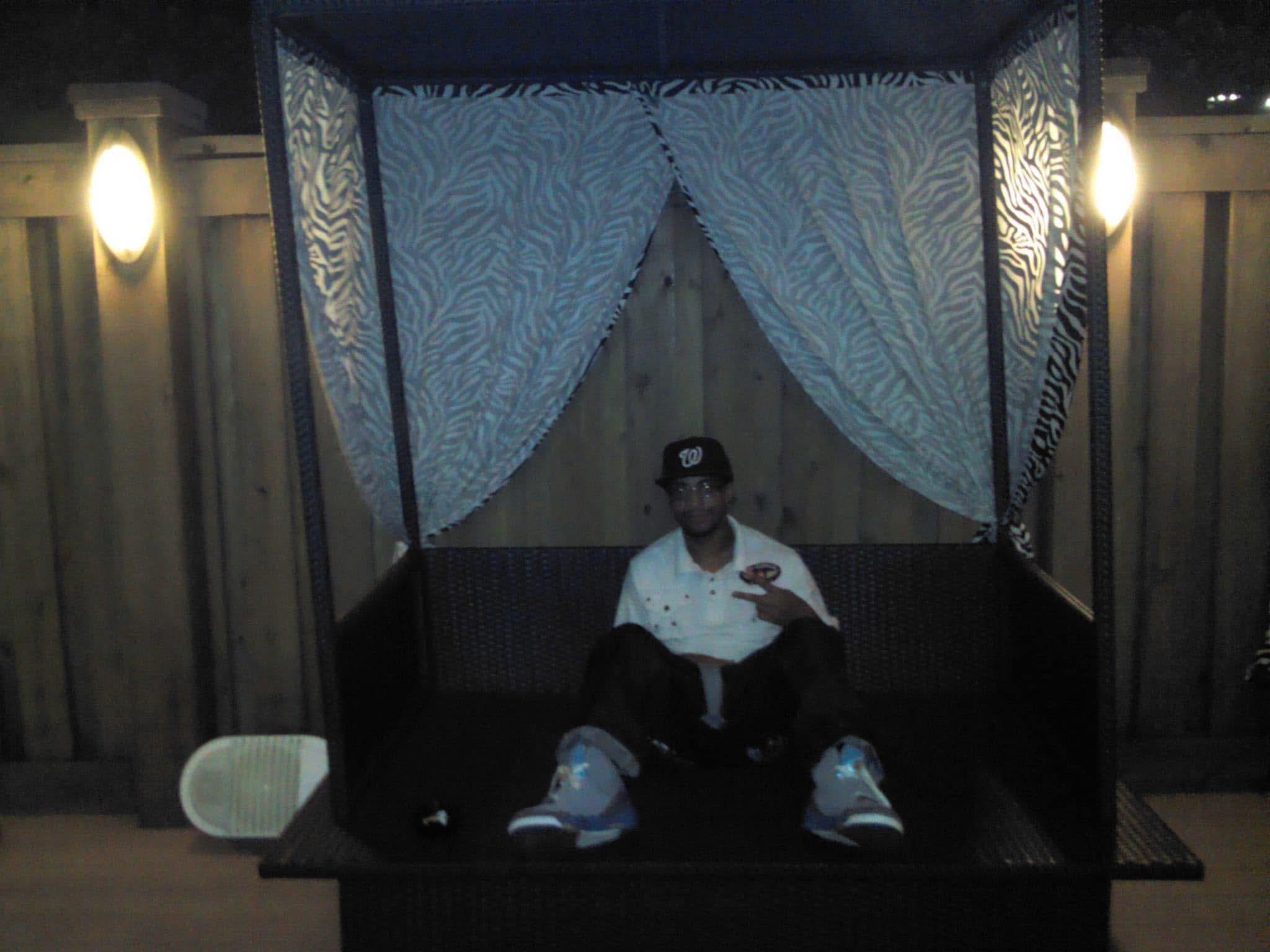 A young man sits comfortably in a chic outdoor seating area at night, enjoying the relaxed ambiance.