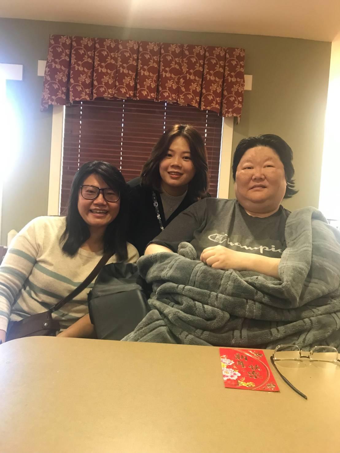 Three friends pose together with smiles as they enjoy each other's company in a warm indoor space.