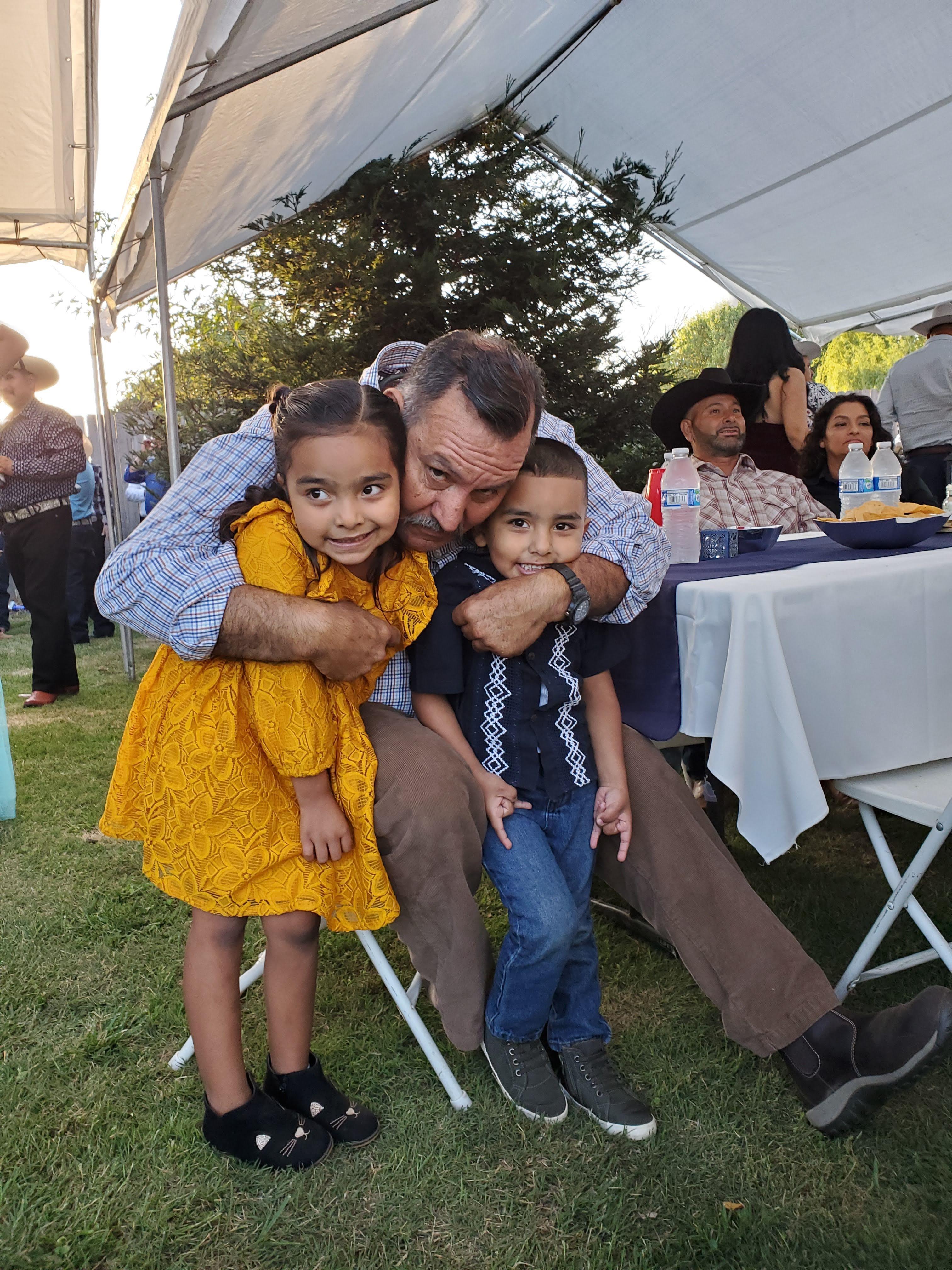Kids hug their grandpa at a family gathering on a festive evening outdoors.
