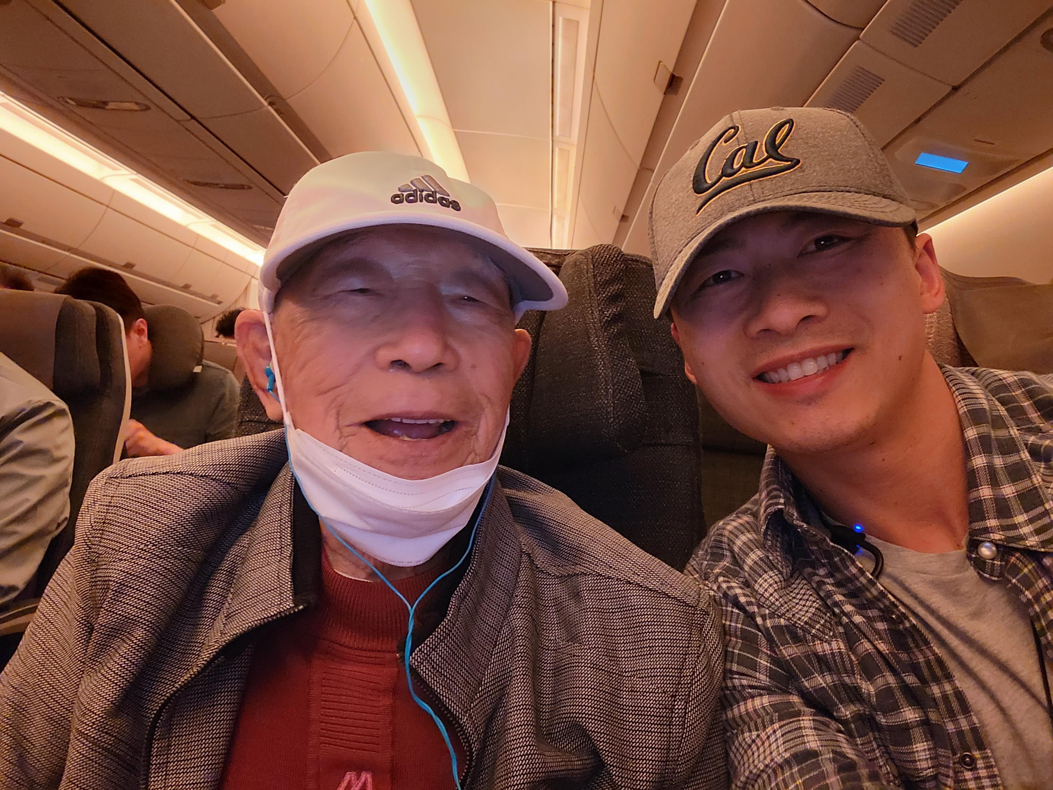 Two men sit side by side on an airplane, smiling and enjoying conversation during the flight.