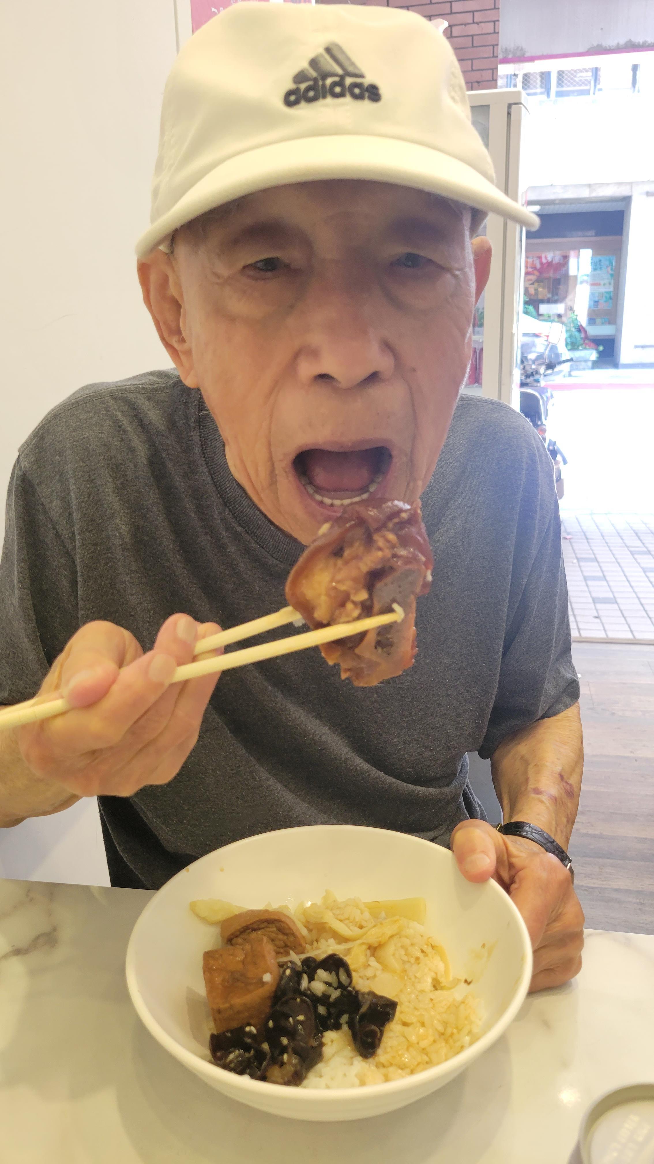 An elderly man happily eats a hearty meal using chopsticks in a charming restaurant.