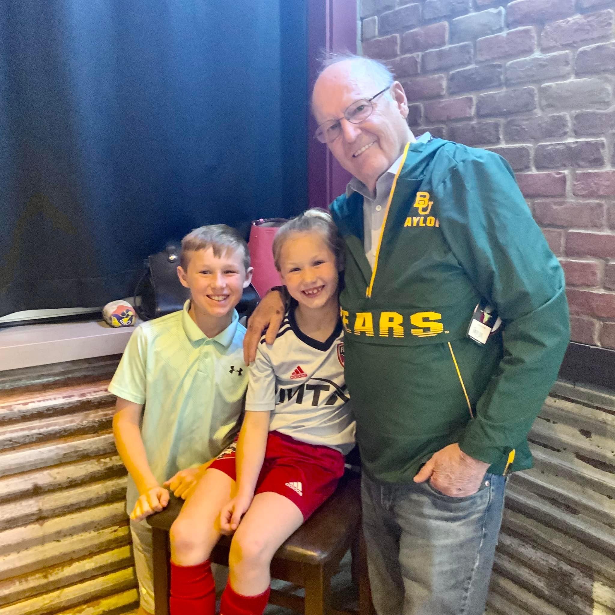 Two children smile with their grandfather in a relaxed environment, enjoying quality family time.