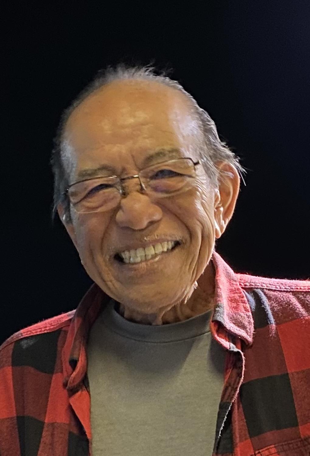 Elderly man with glasses smiles widely, creating a warm atmosphere in a casual indoor environment.