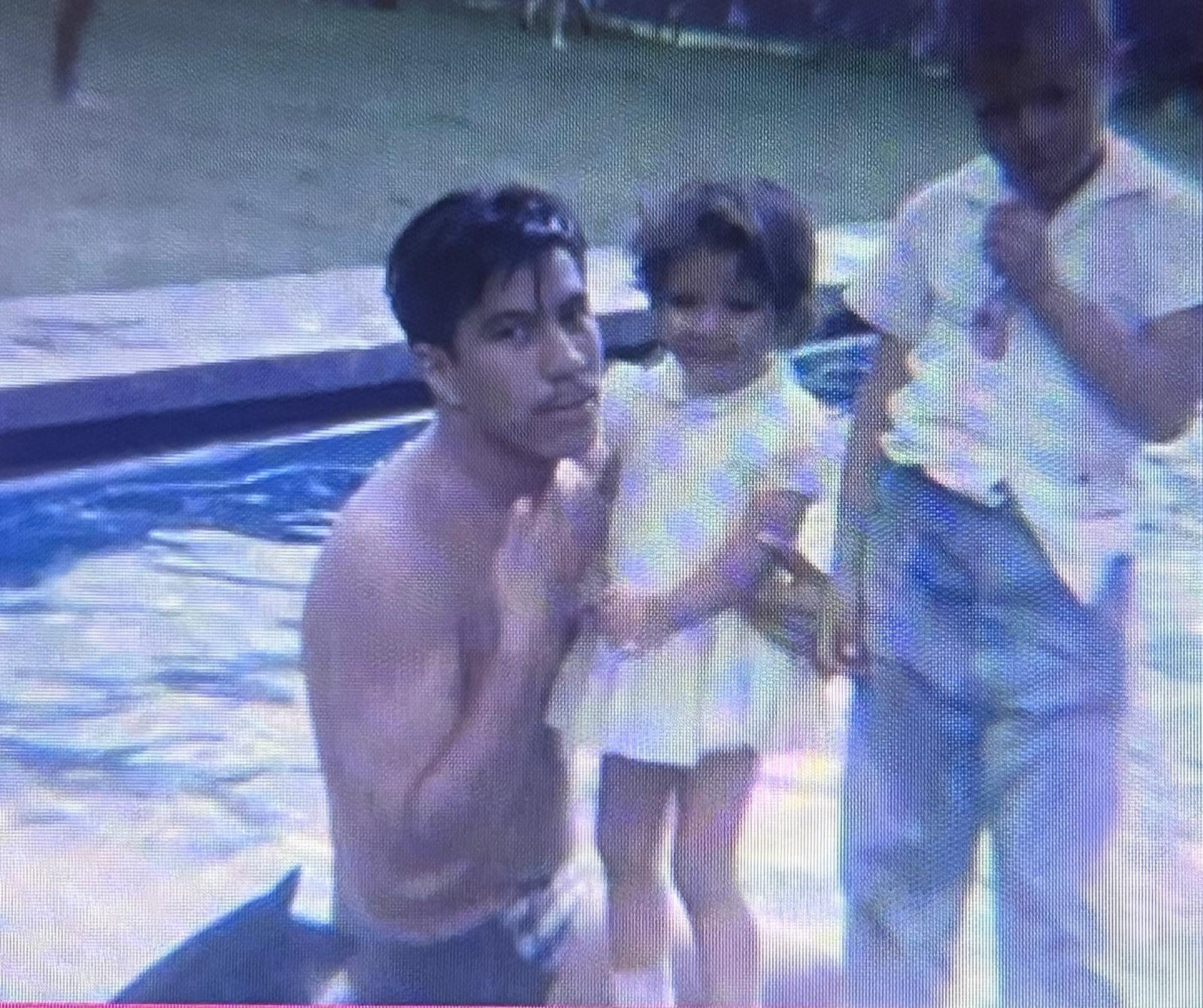 A father holds his young daughter while a son stands nearby, all enjoying their time at the pool.