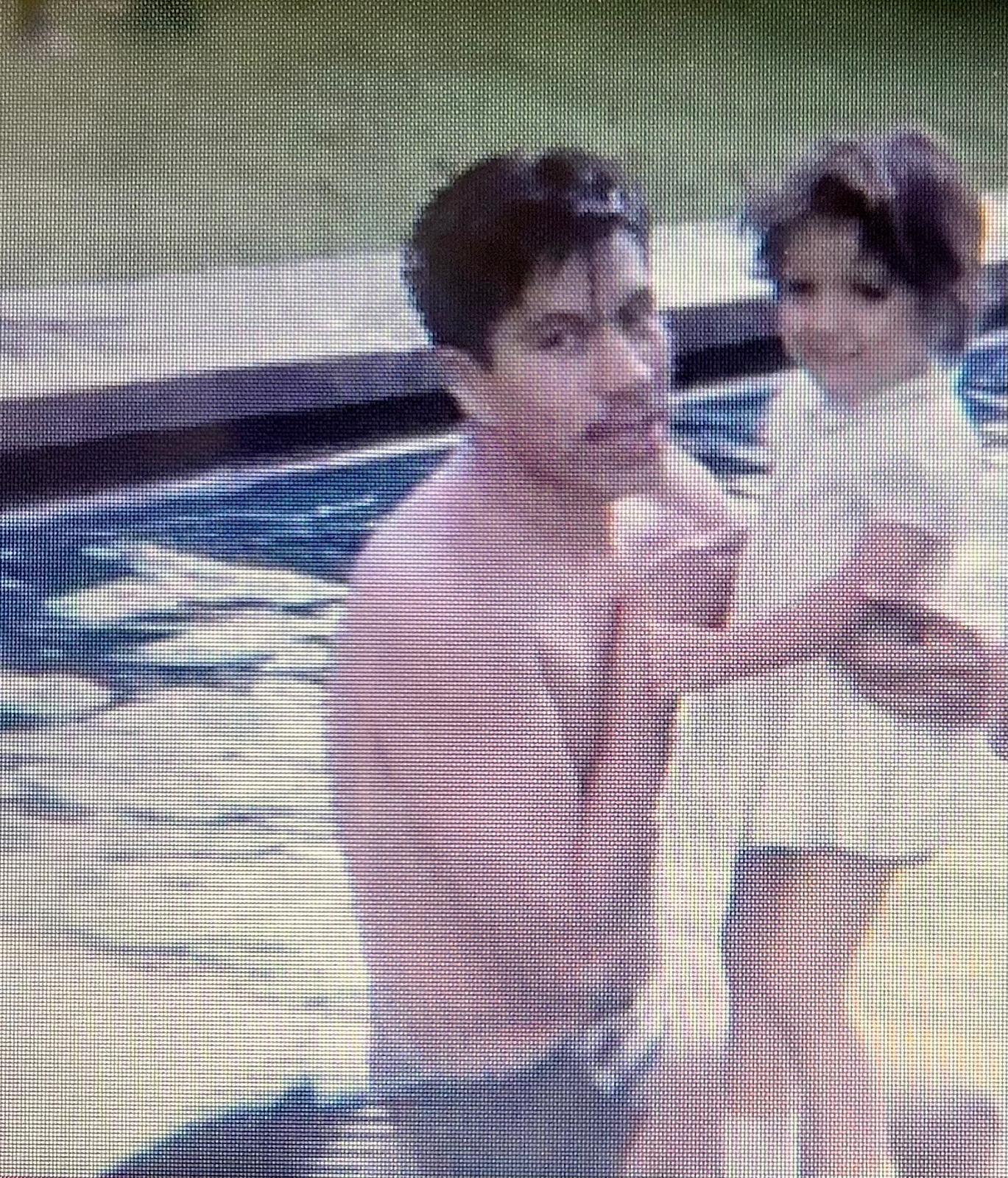 A father embraces his young daughter in a swimming pool, both enjoying a sunny day together.