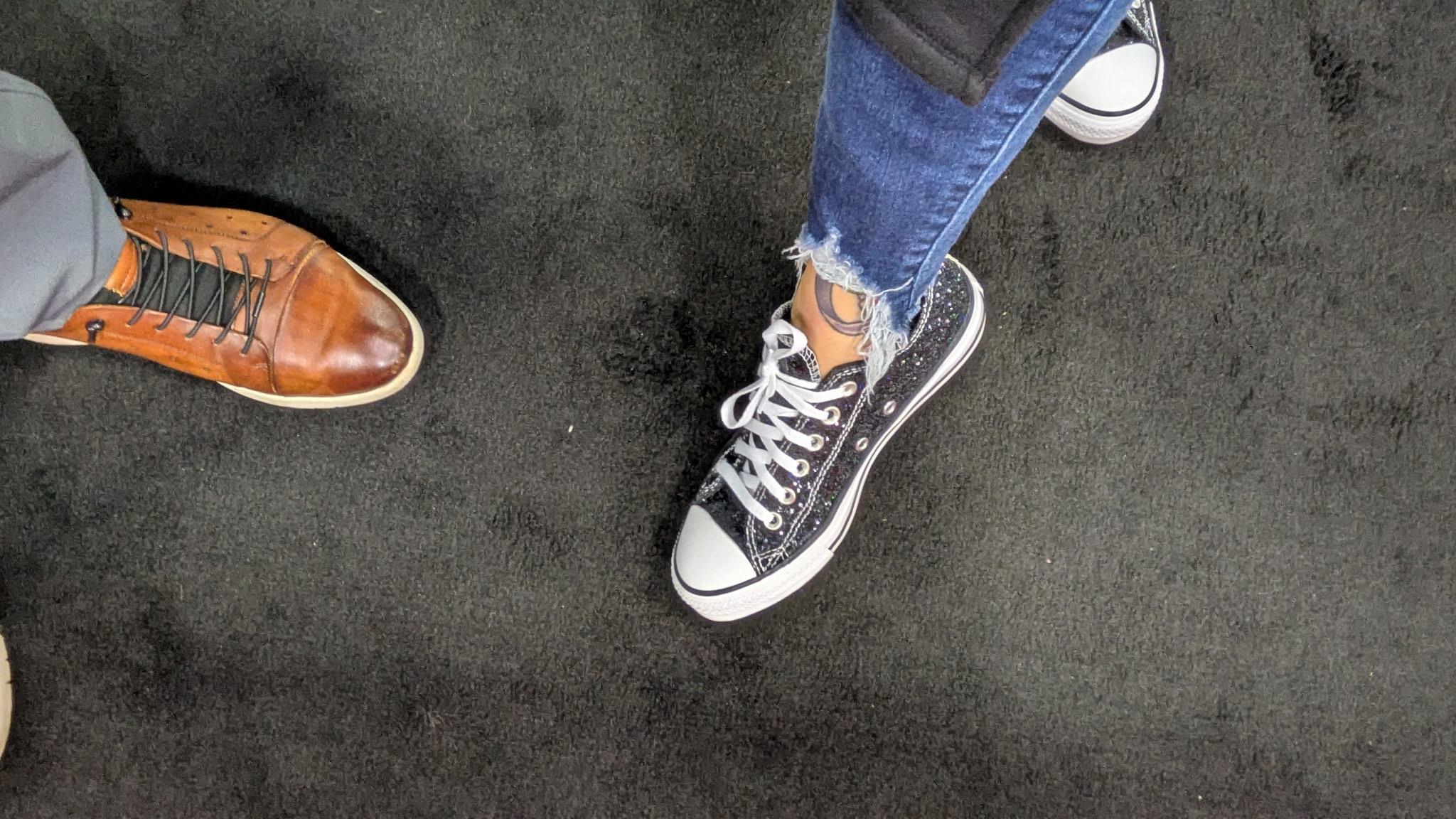 Two pairs of shoes on a black carpet display unique styles and personal expressions at a gathering.