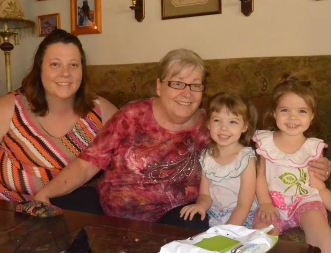 Three women and two girls pose happily together on a couch, showcasing their bond in a warm setting.