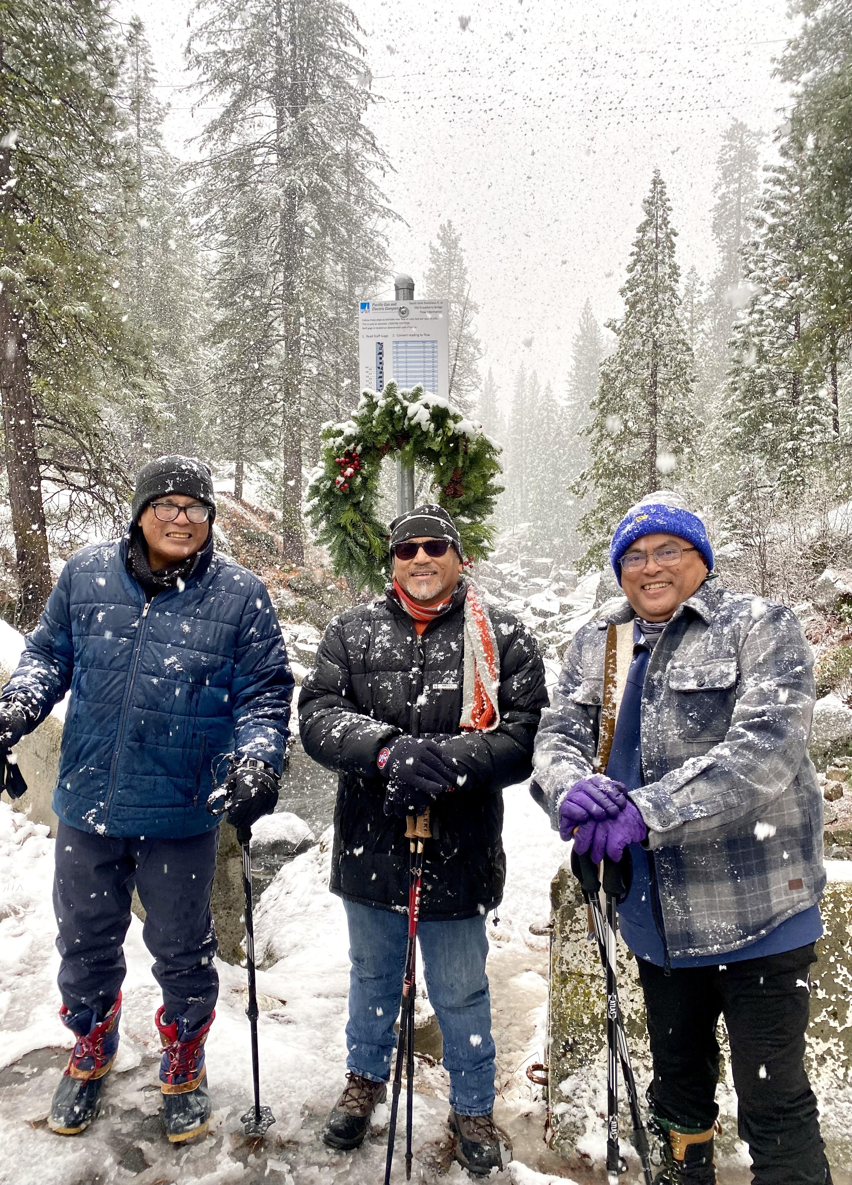 Three friends smile together, bundled up in a snowy winter landscape.