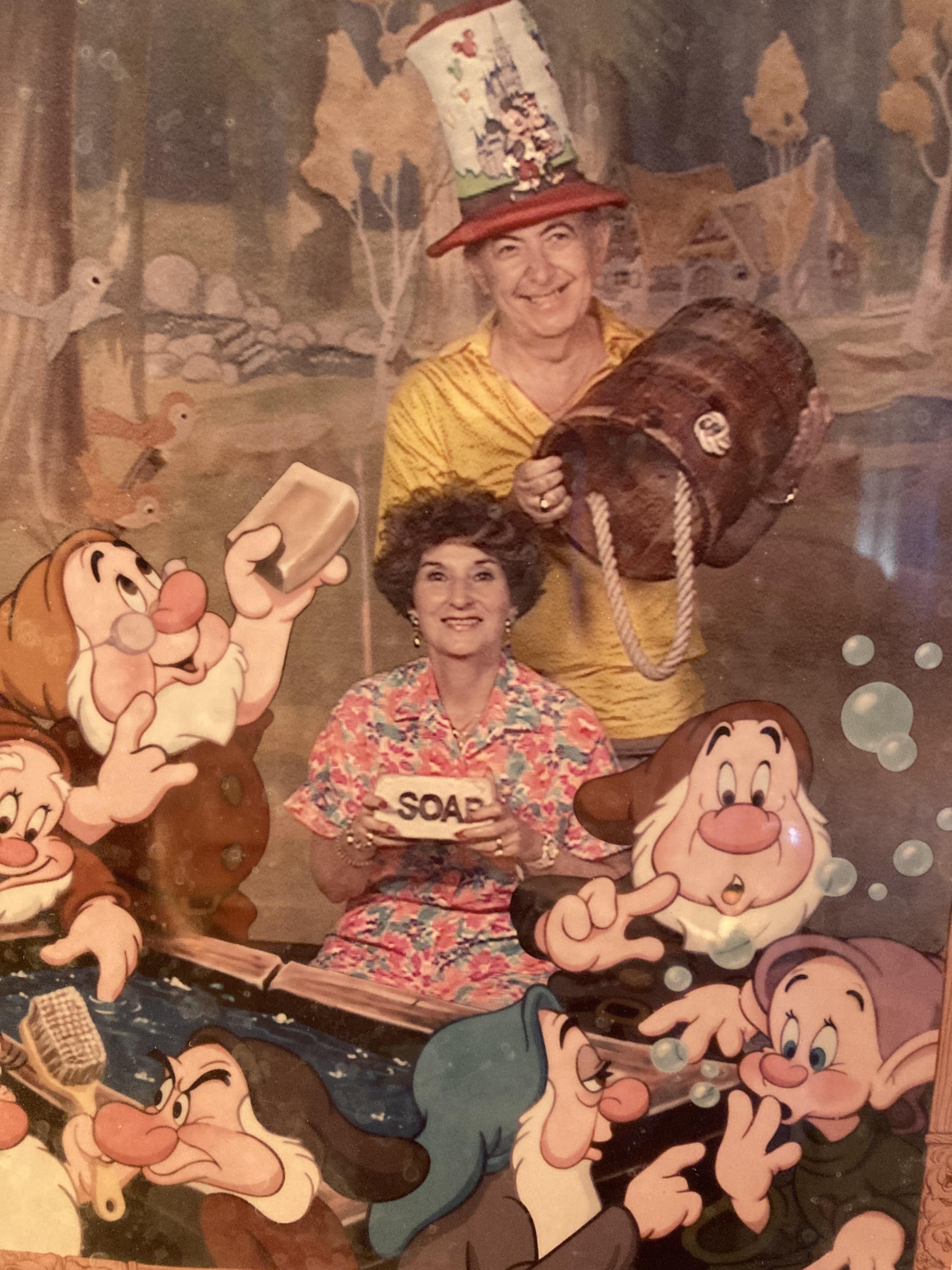 Two people in vibrant costumes smile with cartoon characters in a joyful setting.