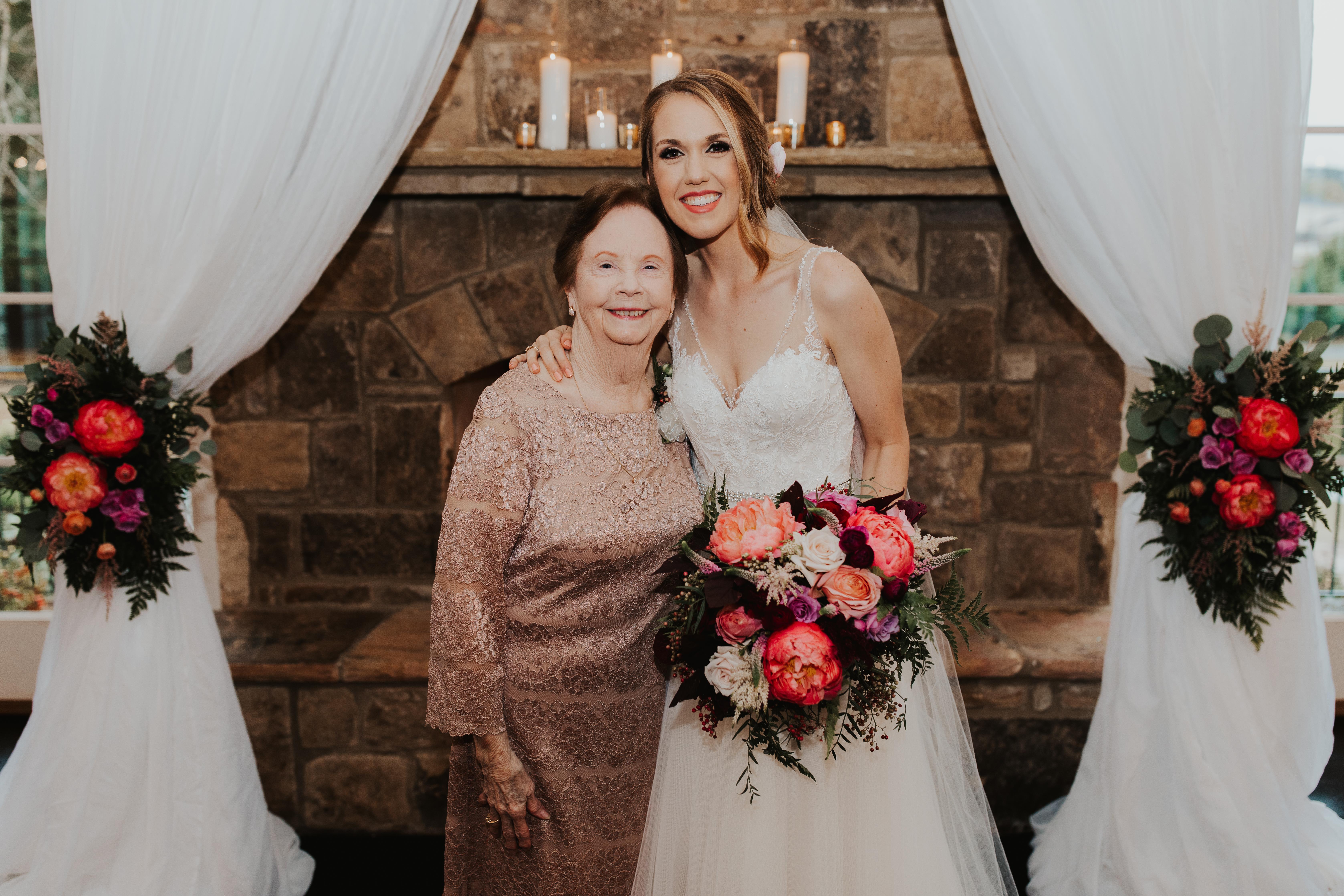 Bride smiles with her grandmother in a decorated wedding venue with flowers and candles.
