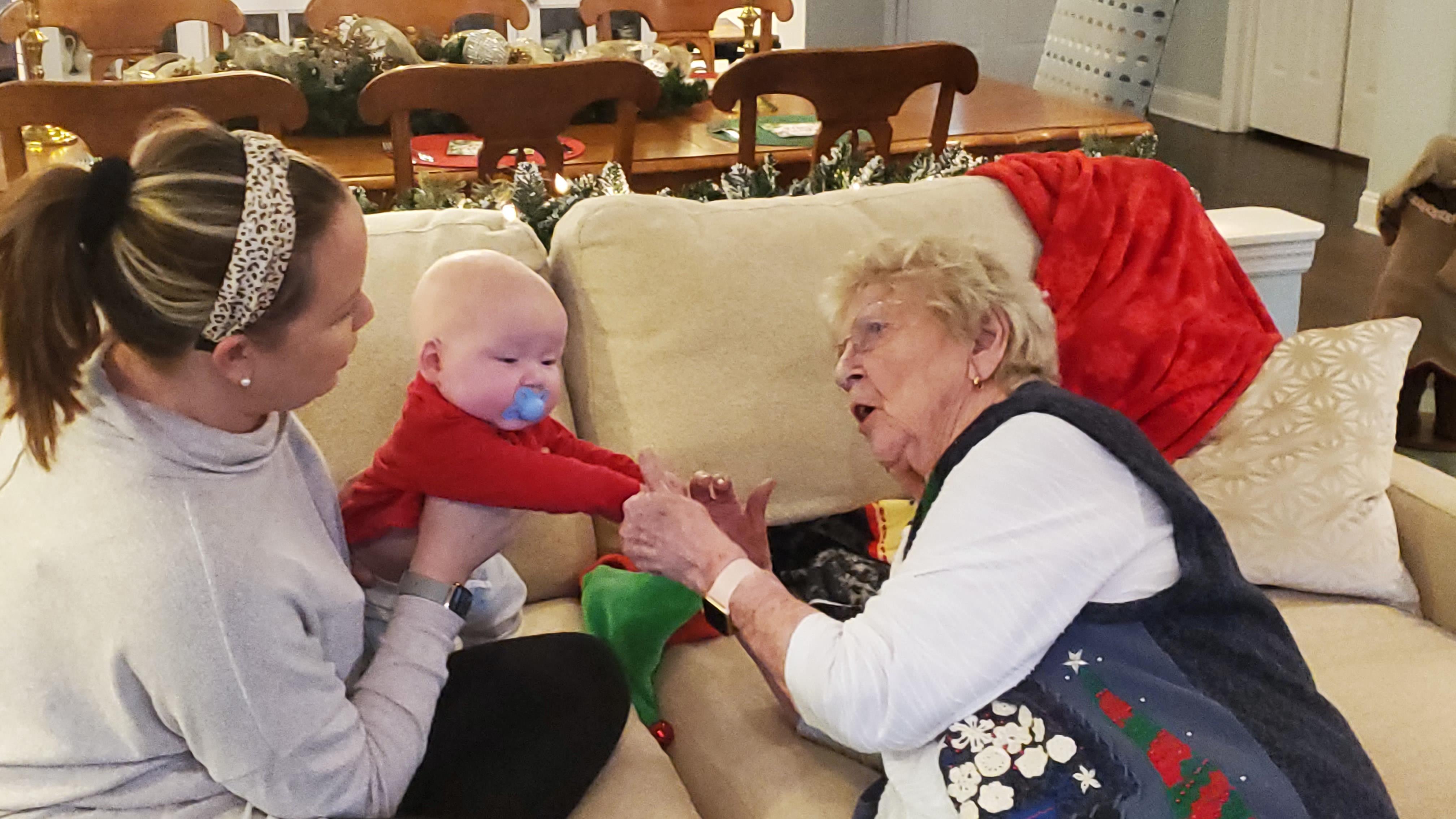 A woman engages with her baby while sitting beside an elderly lady who enjoys the moment.