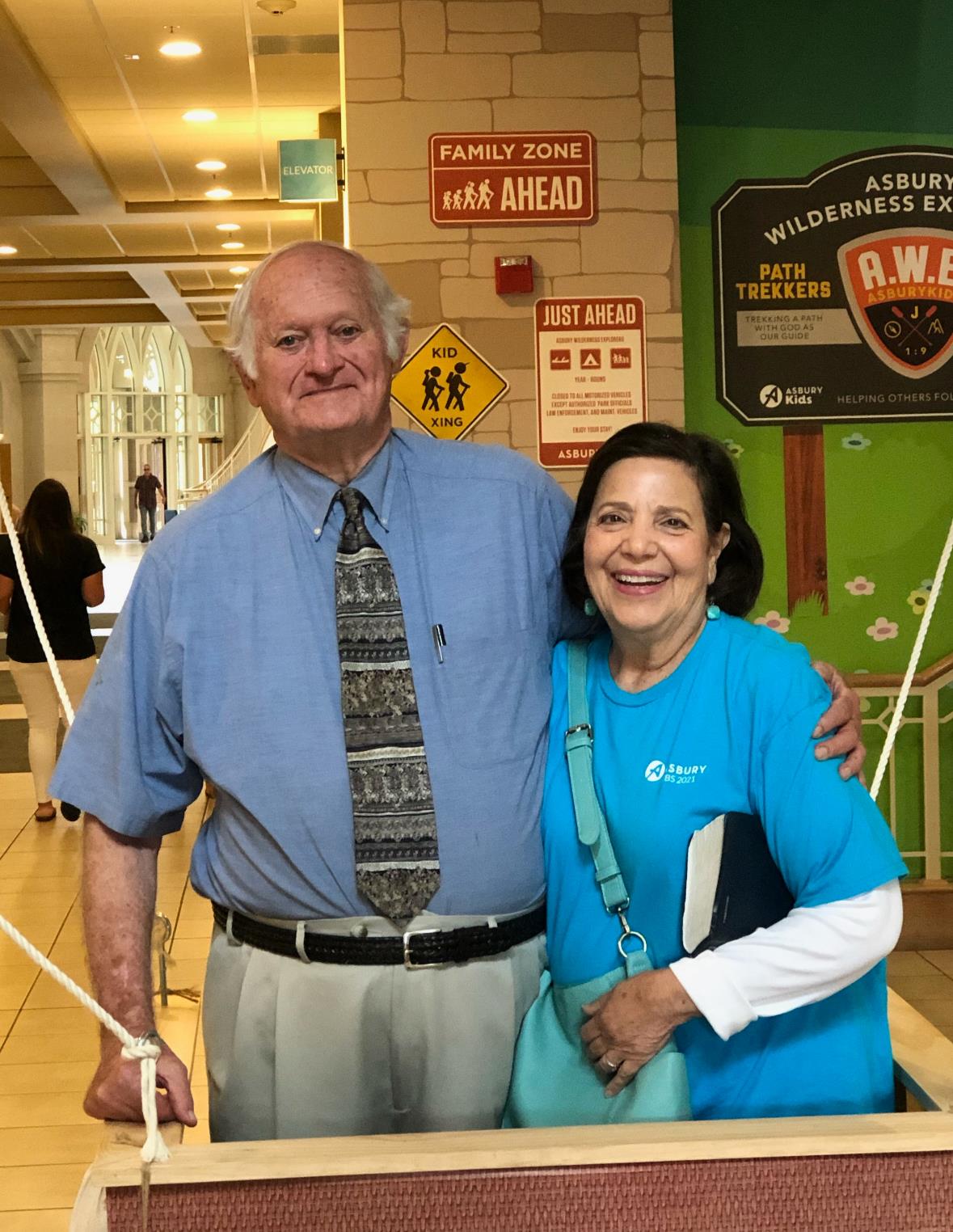 Two older adults, a man and a woman, pose happily in a lively location filled with signs.