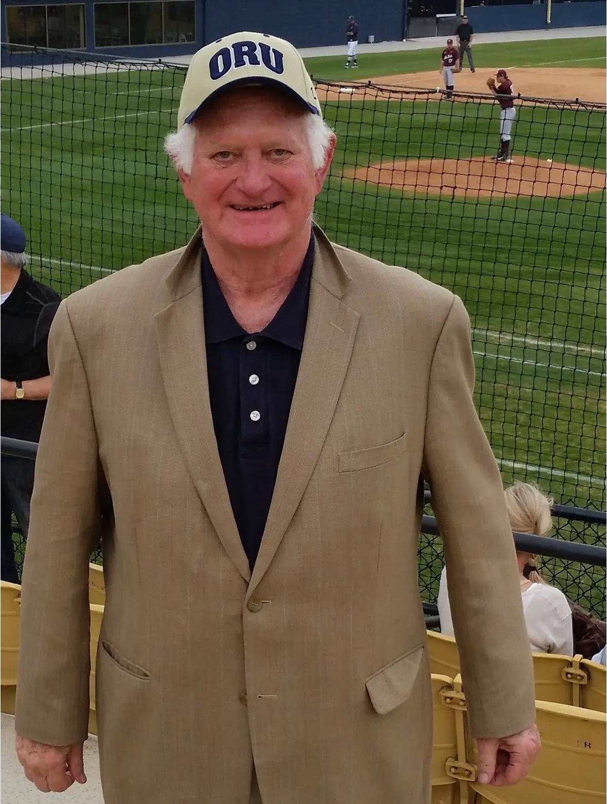 Cheerful older gentleman in a suit and cap enjoys a baseball game at Oklahoma Christian University.