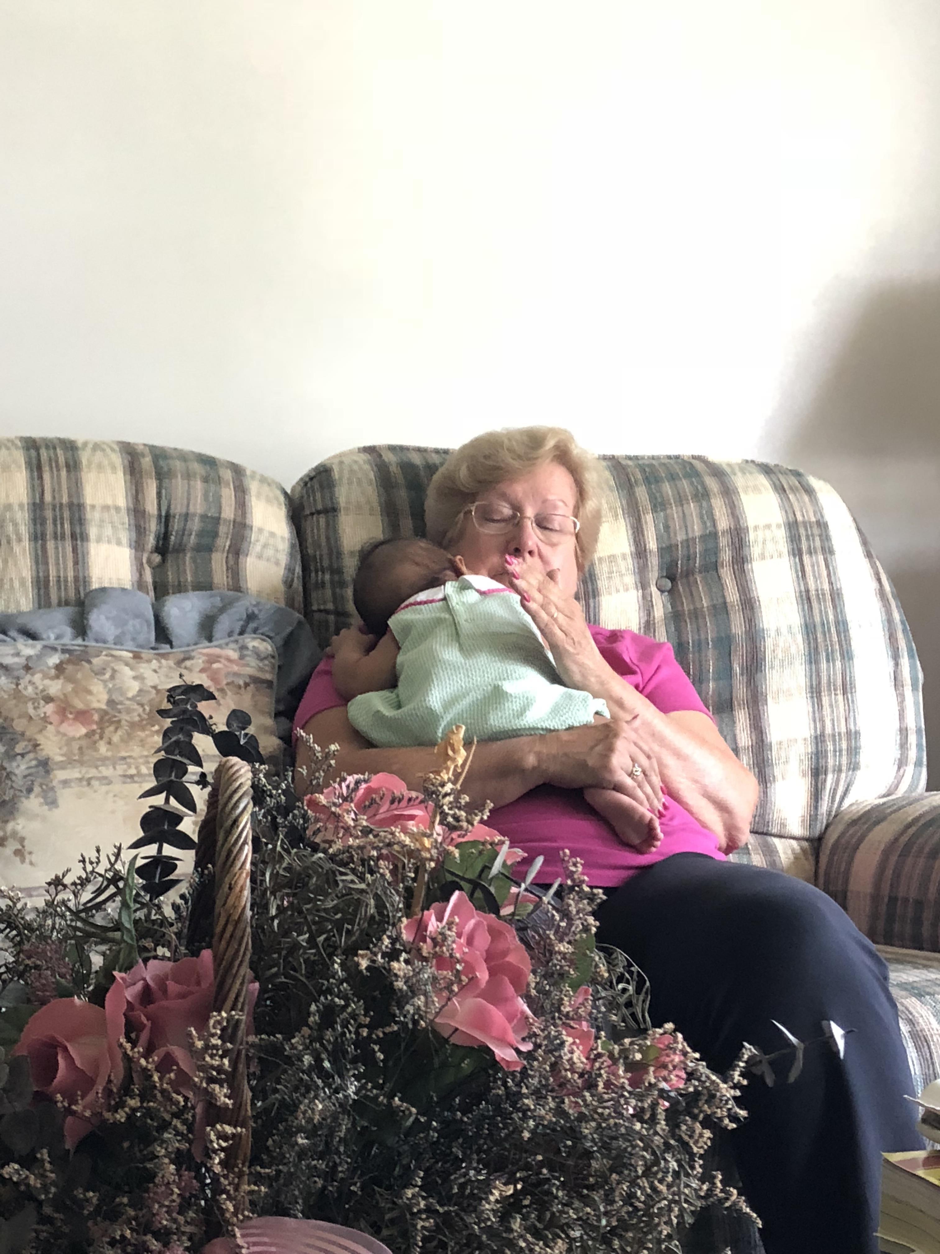 An elderly woman joyfully holds a newborn baby in a comfortable living room setting.