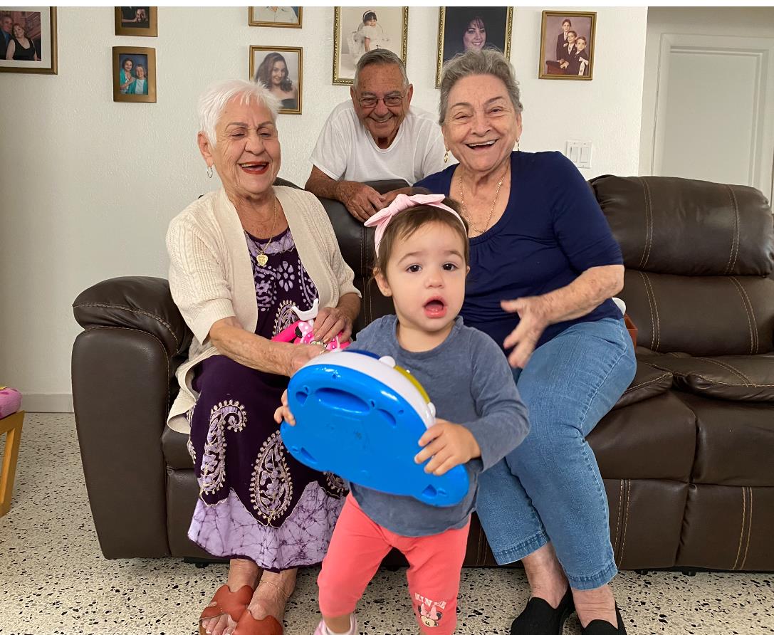 A joyful family gathering features a young child engaged with a toy while relatives smile nearby.