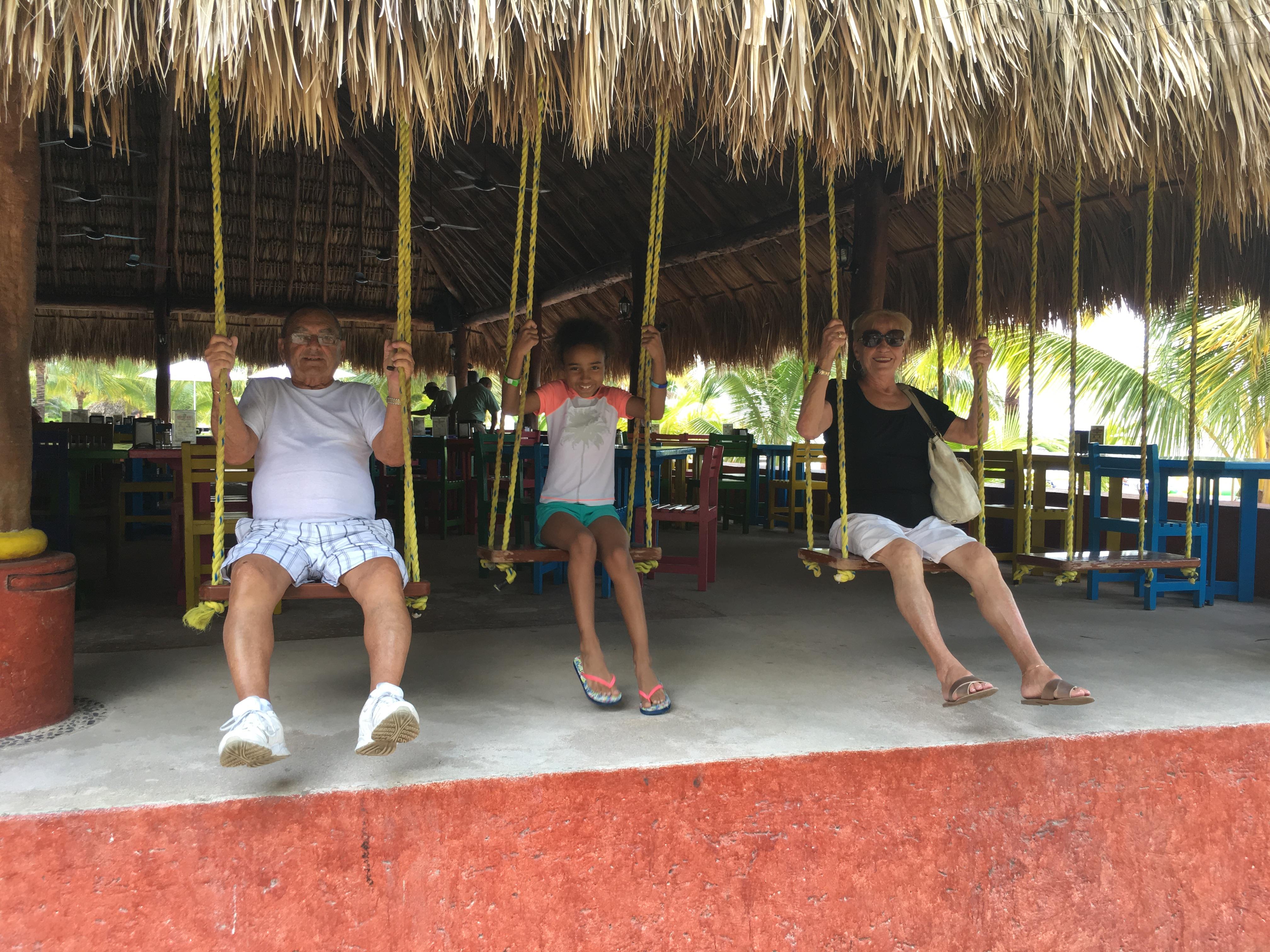 Three individuals sit on swings at a beach restaurant, enjoying a relaxing moment by the ocean.