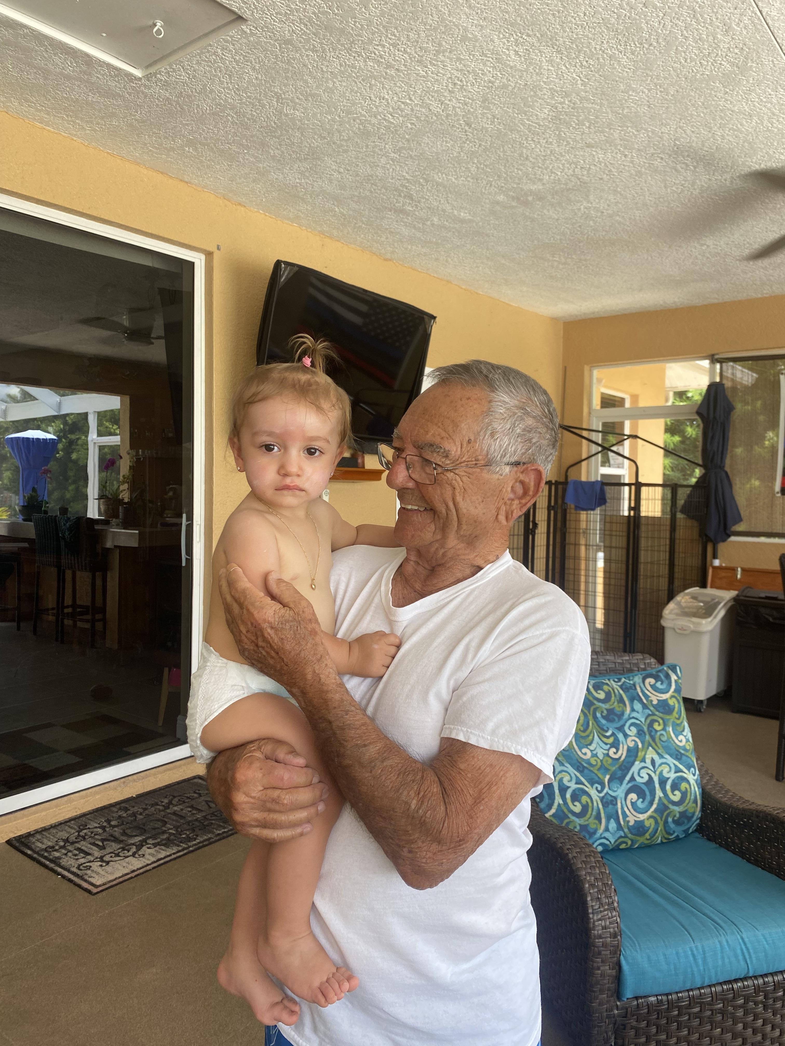 A happy grandfather embraces his baby granddaughter by the pool, enjoying their time together.