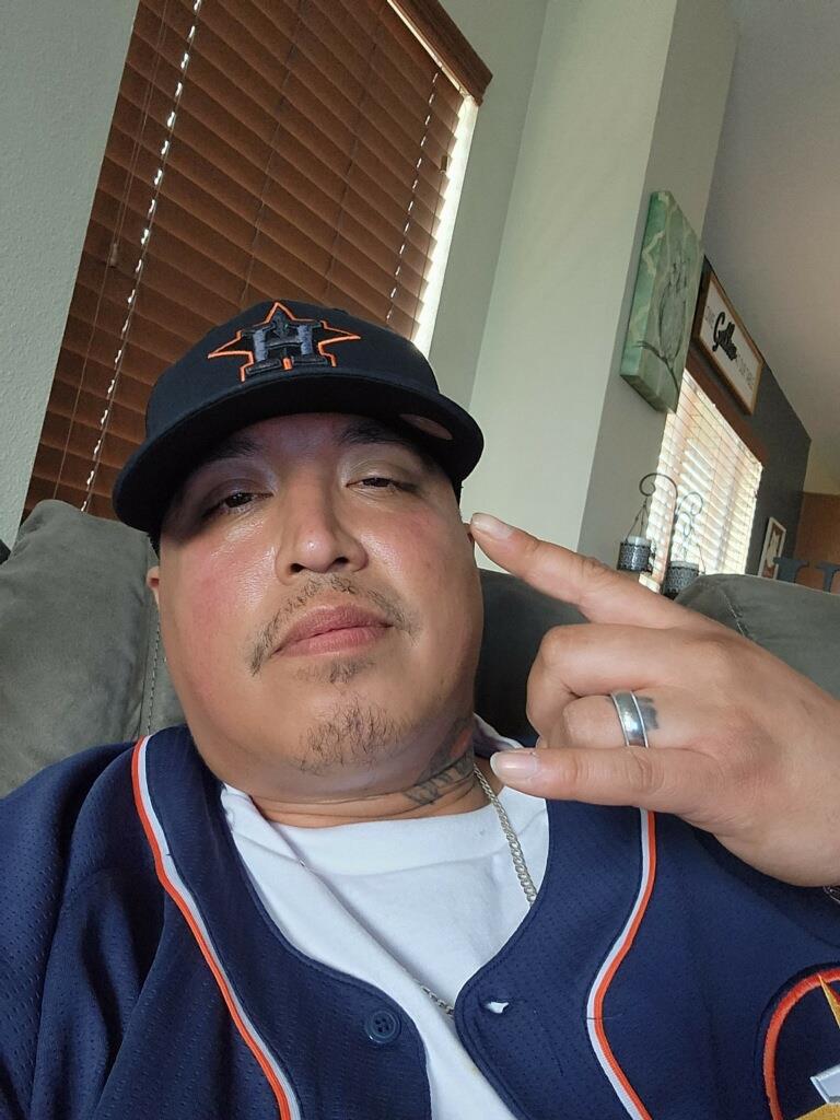 Individual poses with a hand gesture while sitting comfortably on a sofa at home.