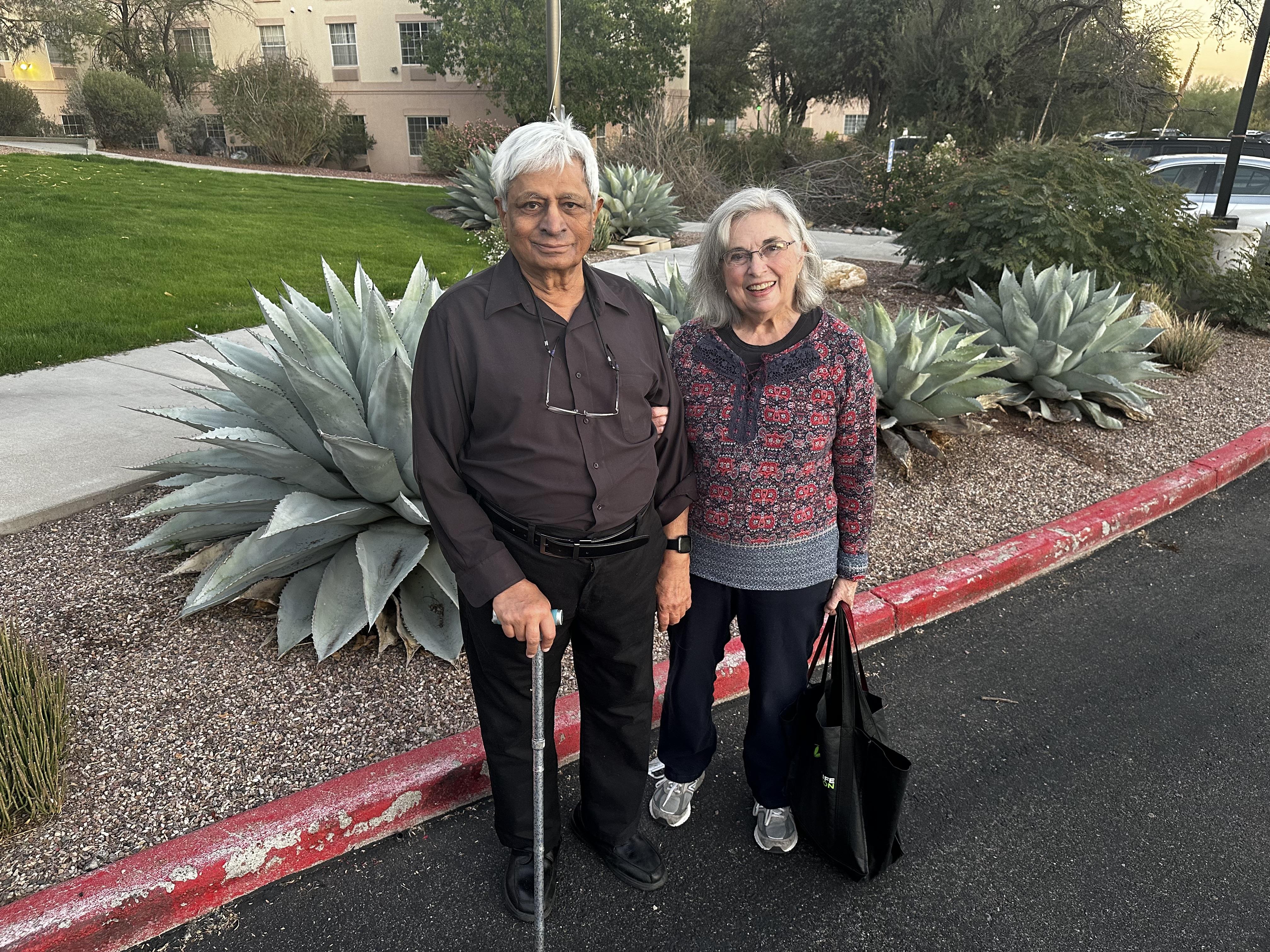 Couple stands together by succulents, smiling happily during a late afternoon stroll.