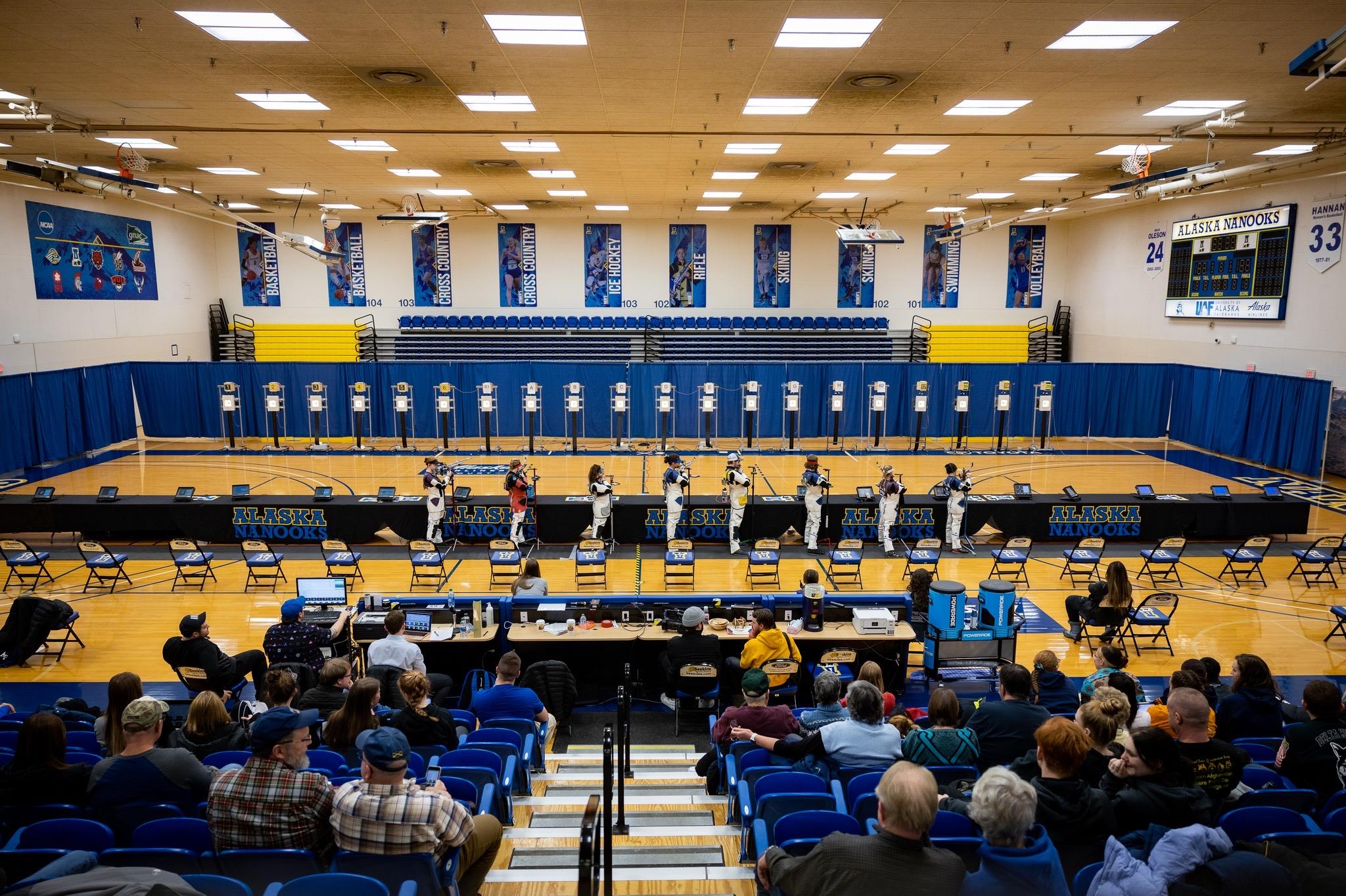 Participants compete in a quiz event inside a gymnasium filled with spectators at a school setting.