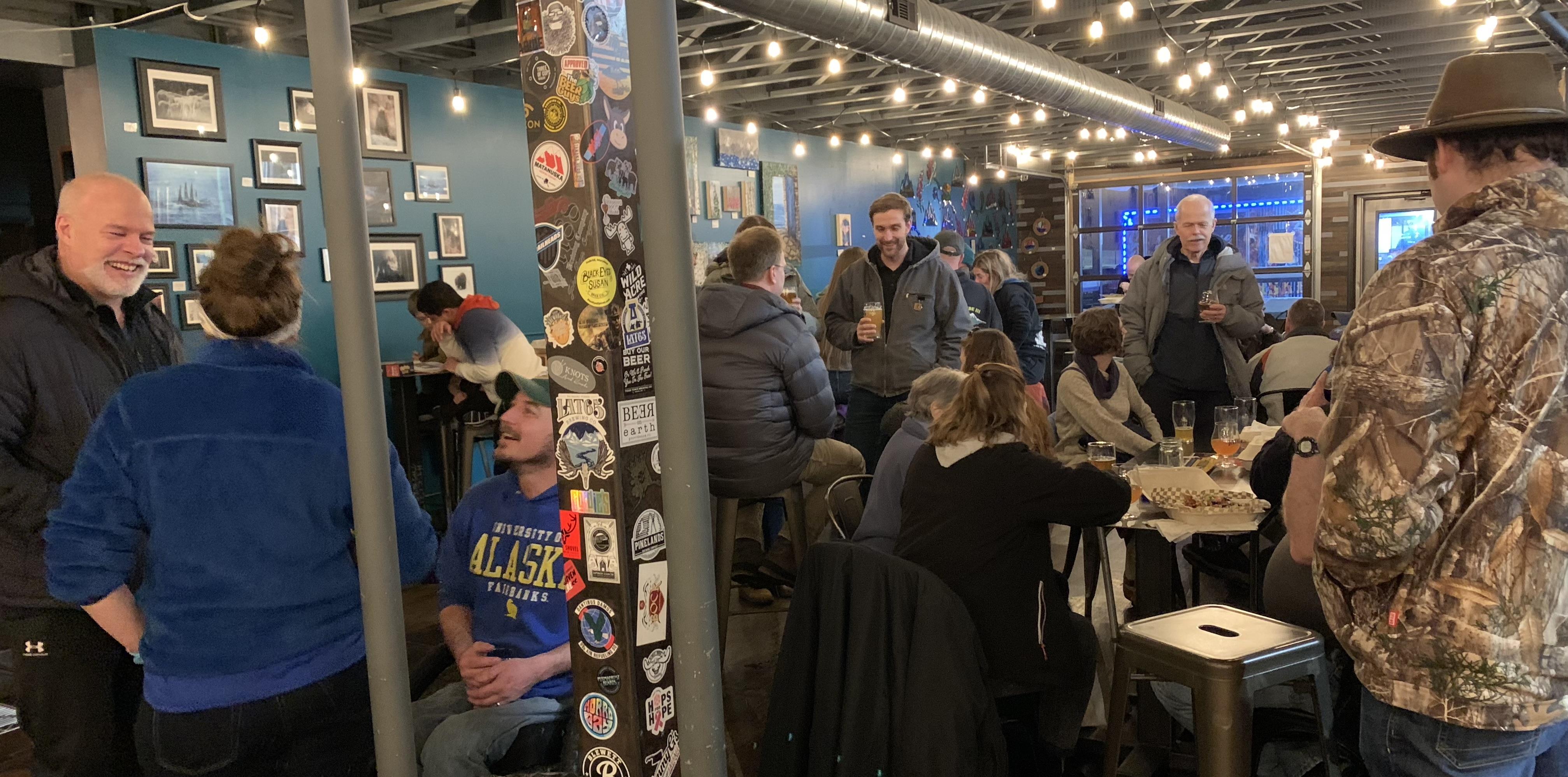 People engage in conversation and enjoy drinks at a brewery during a winter evening.
