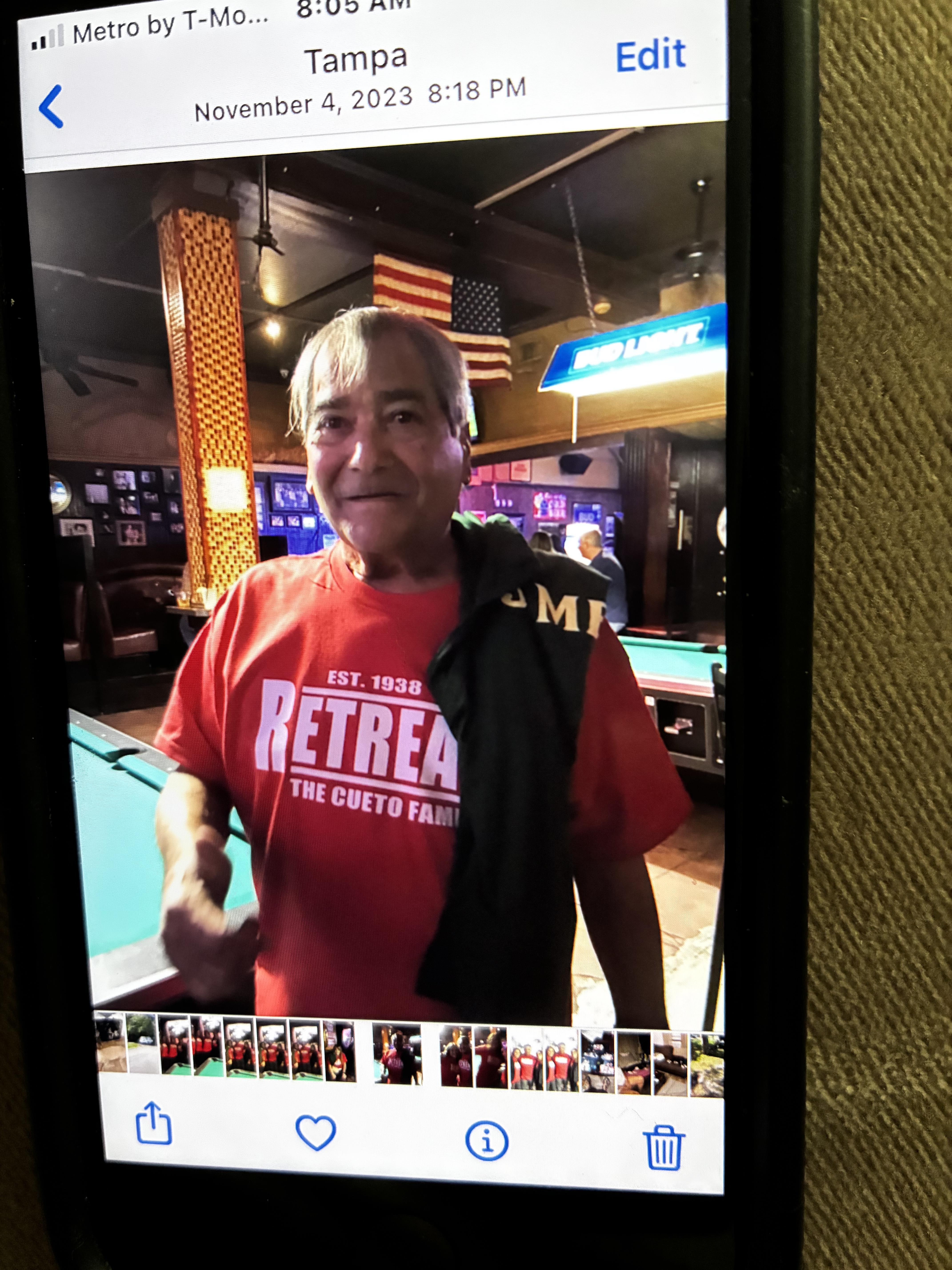 A patron smiles and gestures while wearing a red shirt in a lively local bar in Tampa.