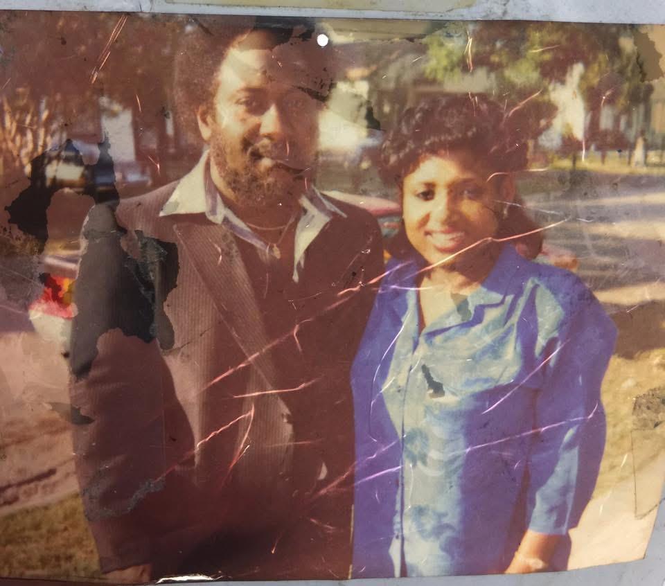 Two individuals stand close together with smiles, enjoying a bright day in a park.