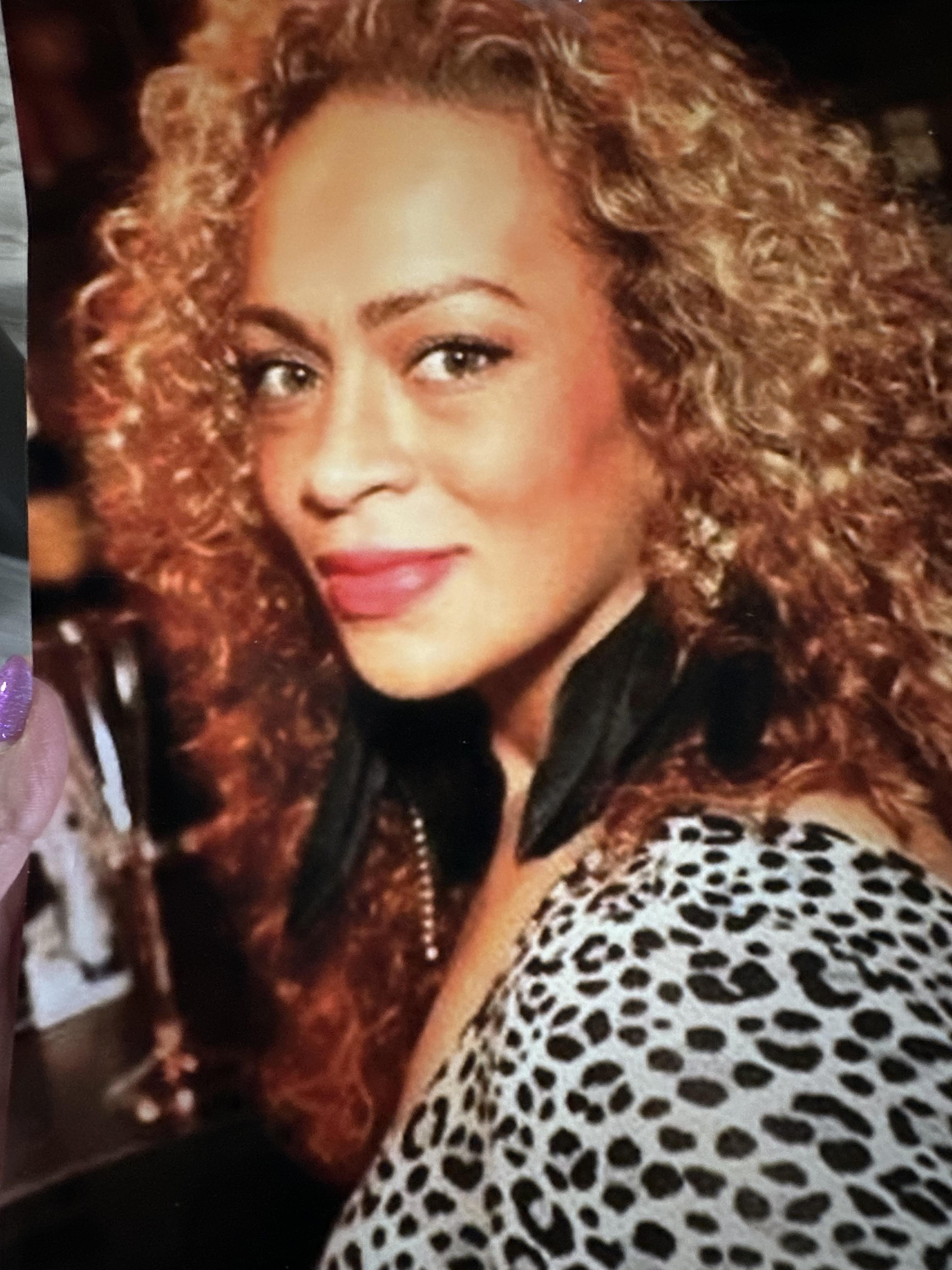 A woman with curly hair enjoys a social gathering, adorned in animal print and bold earrings.