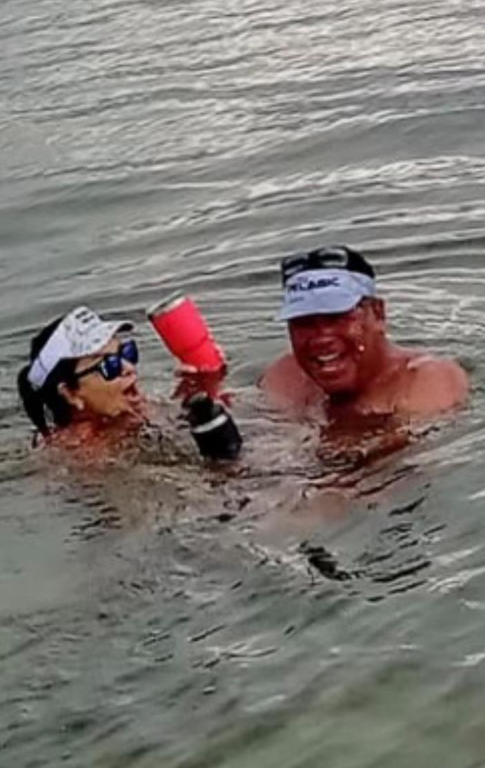 Two men are playfully splashing in the water while holding colorful cups under the sun.