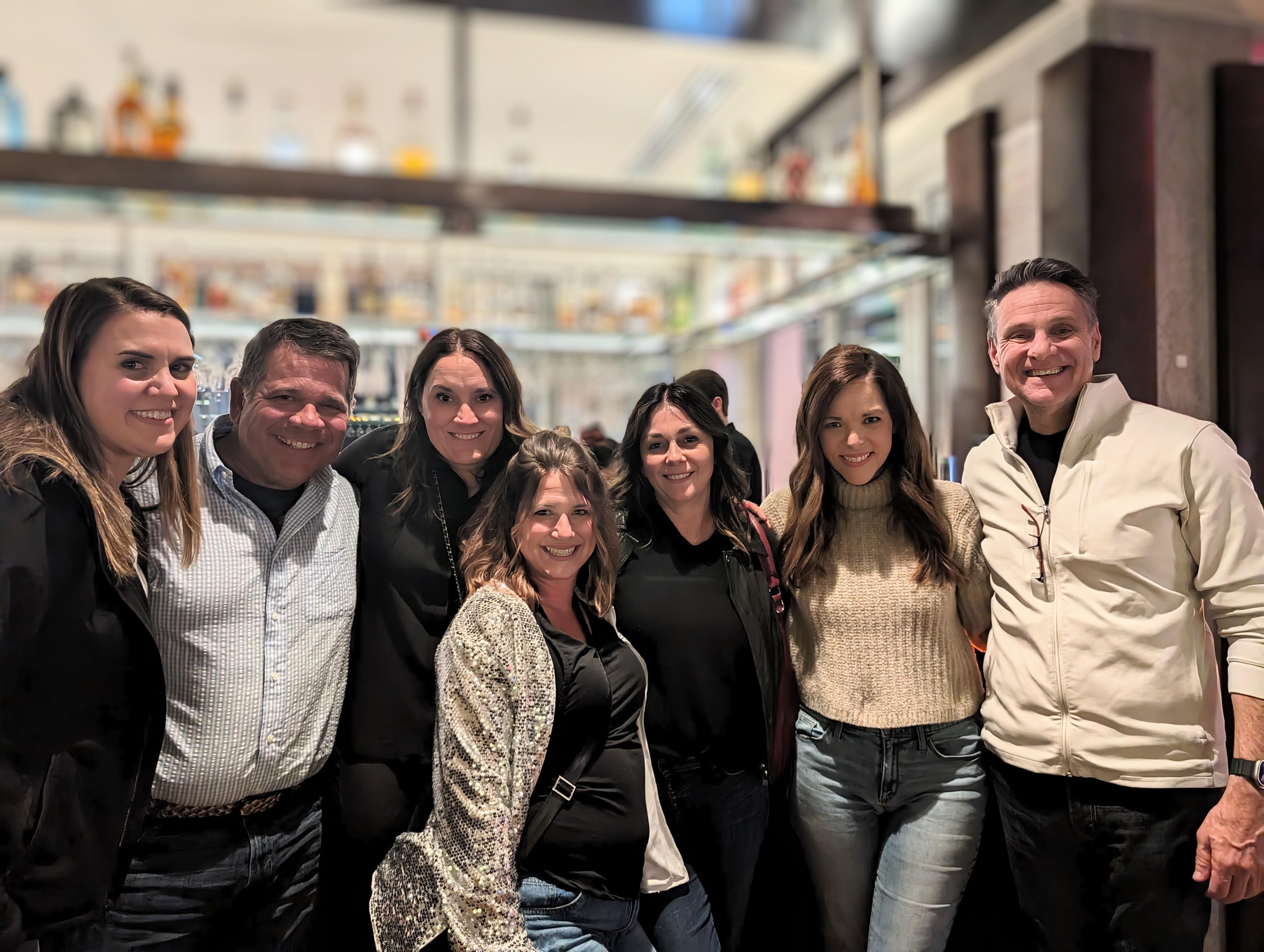 A group of seven friends enjoys their time together at a restaurant, smiling and chatting.