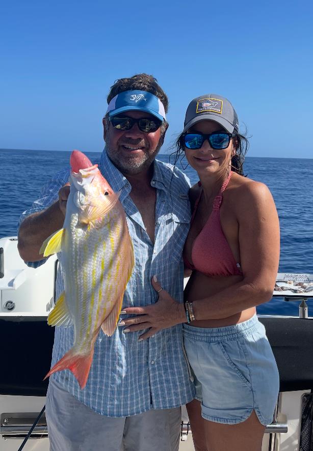 Couple proudly holds a colorful fish while enjoying a sunny fishing trip on the ocean.