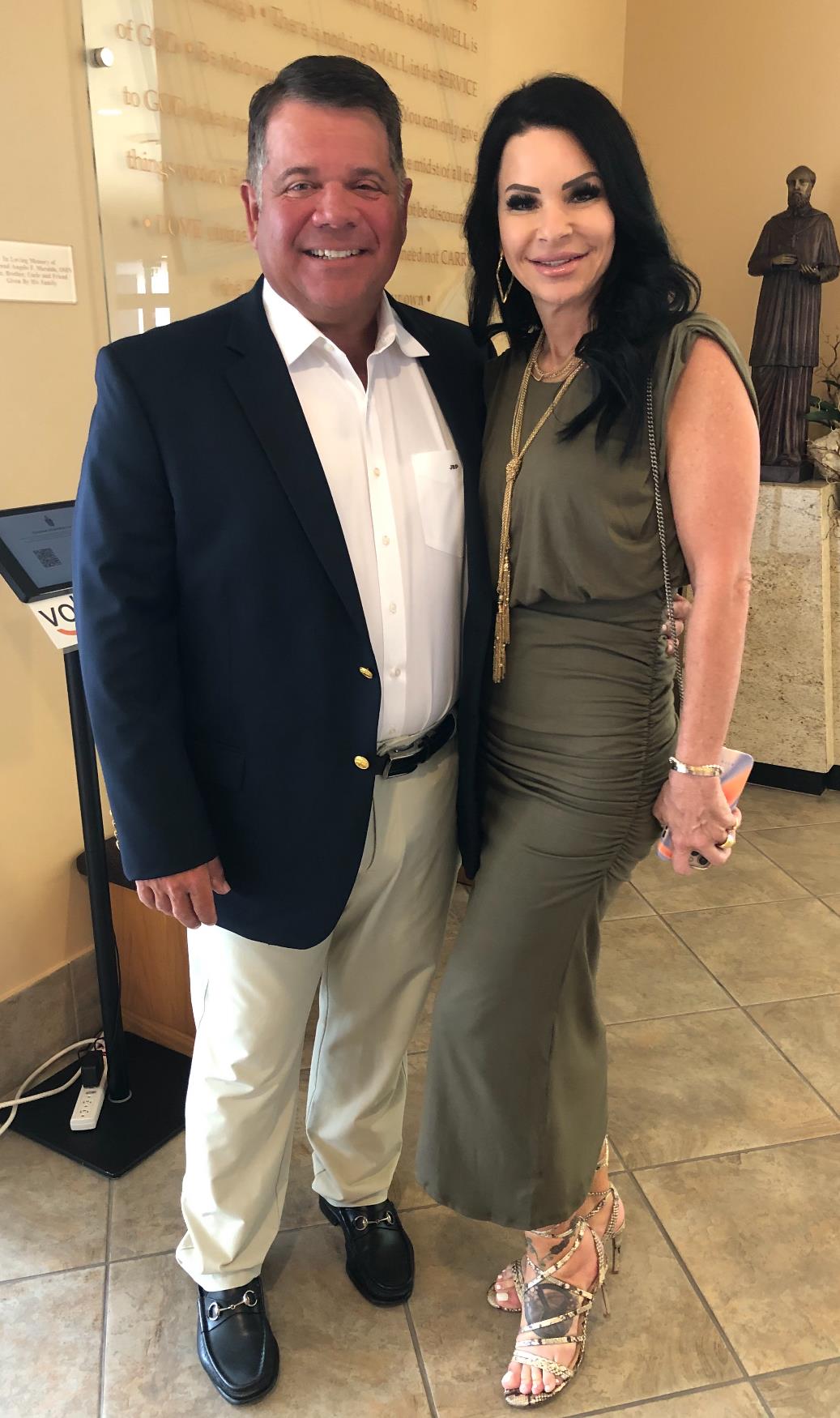 A stylish couple smiles warmly at a social event, highlighting their chic outfits.