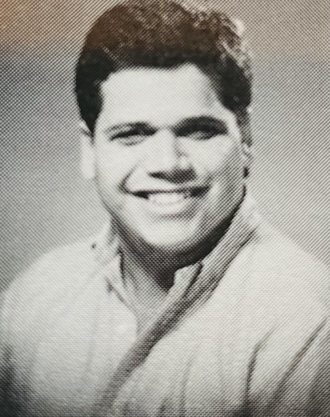 A young man smiles confidently in a collared shirt, set against a plain backdrop.