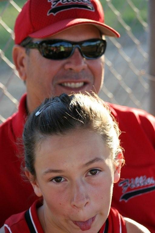 A coach smiles as a young athlete playfully sticks out her tongue at a summer sports event.