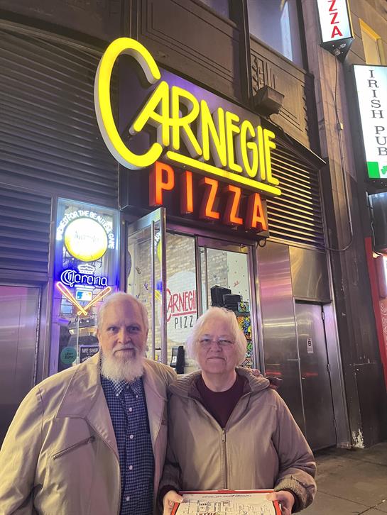 A man and woman standing in front of a pizza restaurant