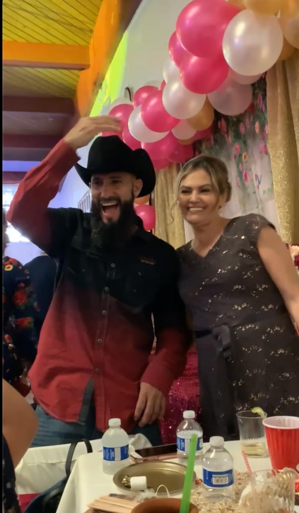 A joyful couple poses together, dressed for a lively celebration filled with colorful decor.