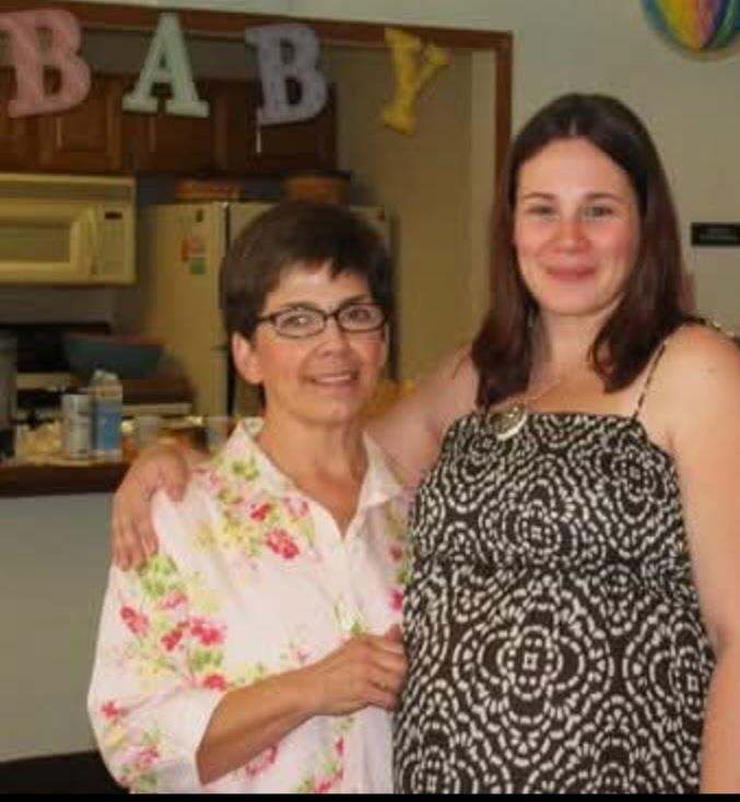 Two women share a joyful moment in a home setting, celebrating the upcoming arrival of a baby.