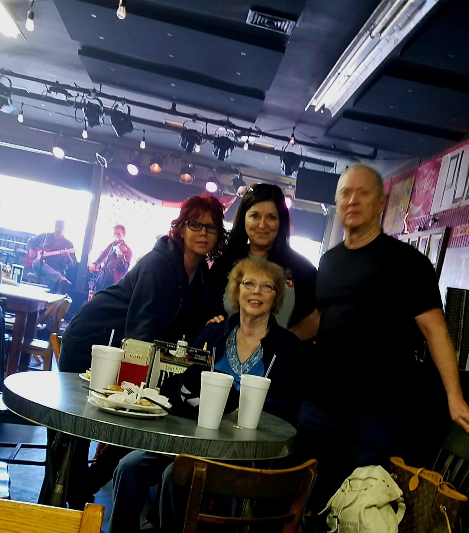 Friends gather around a table, enjoying drinks while watching a live band perform in the background.