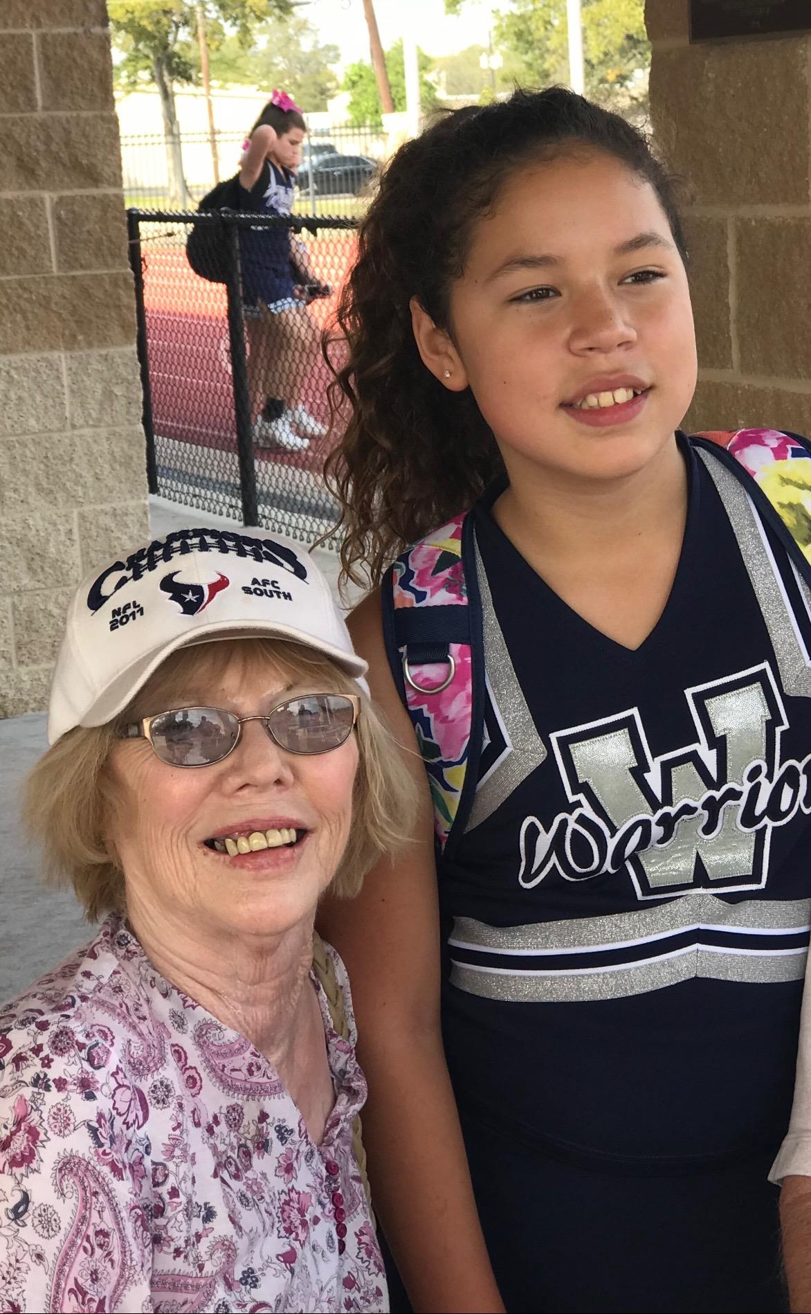 A happy grandmother poses with her granddaughter in cheerleading attire at a sports event.