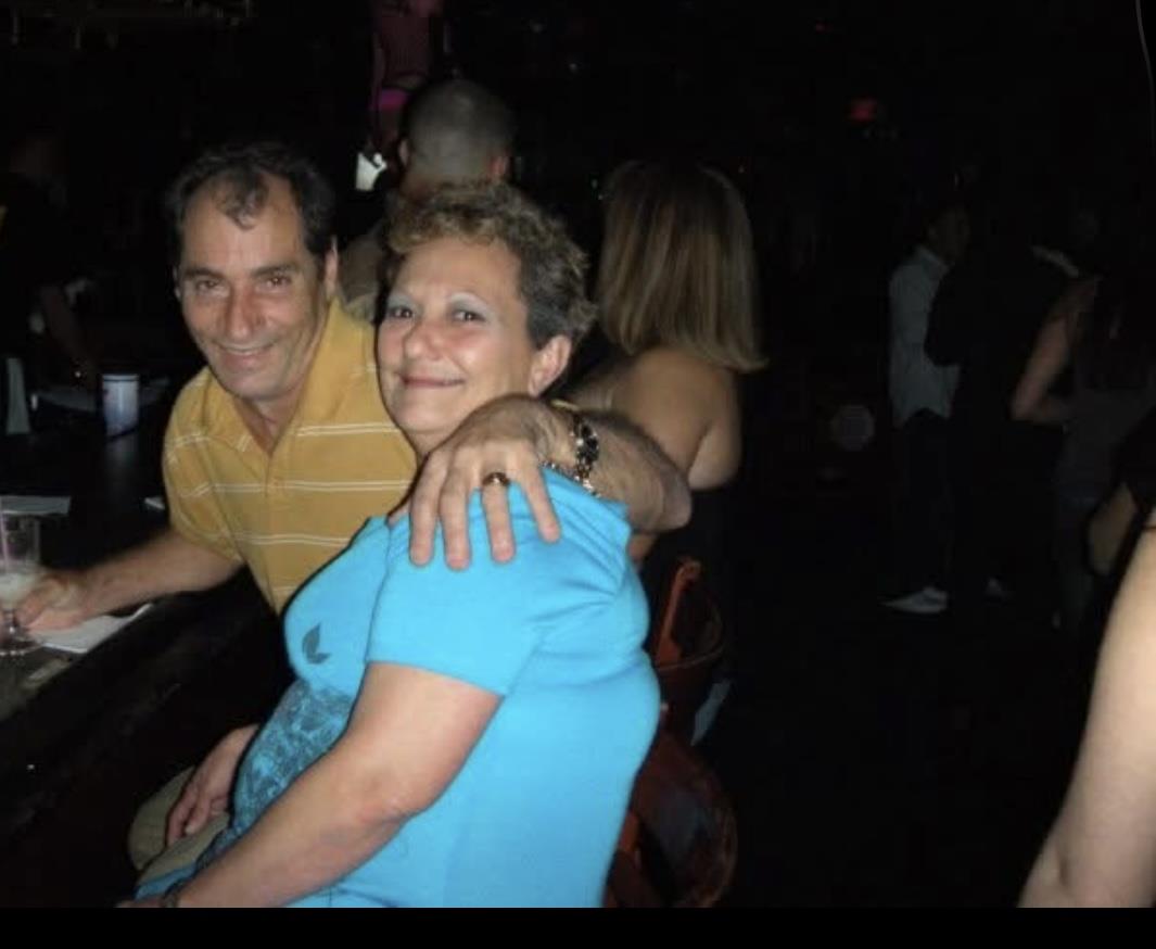 A cheerful couple poses for a photo at a bustling bar while friends are gathered around.