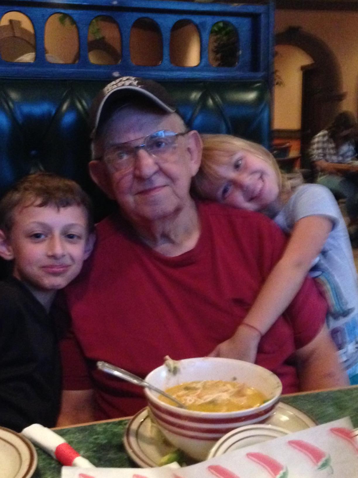 Two joyful children embrace an elder while enjoying a hearty meal together in a lively restaurant.