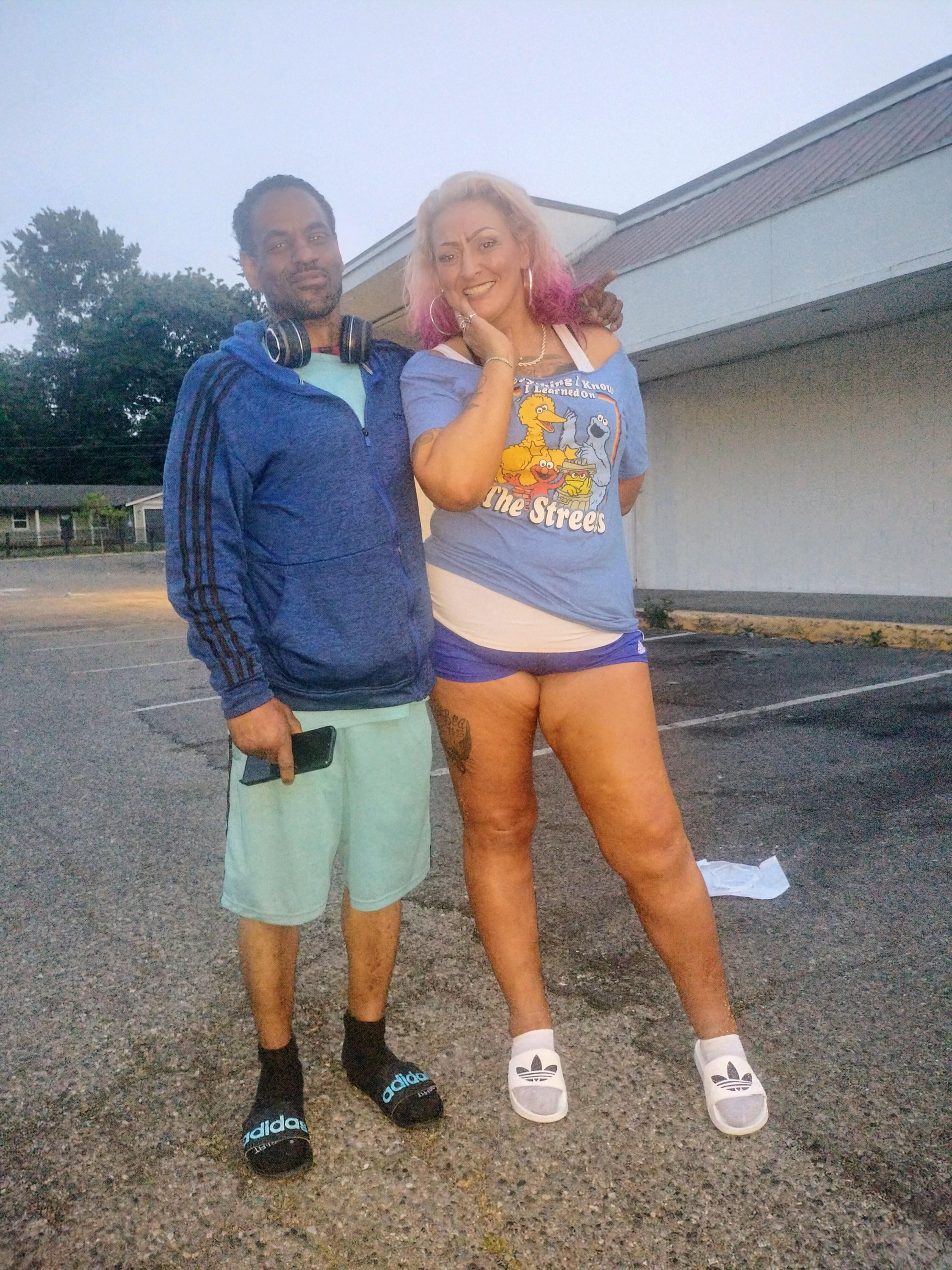 Two individuals stand together smiling, enjoying the relaxed evening atmosphere outdoors.