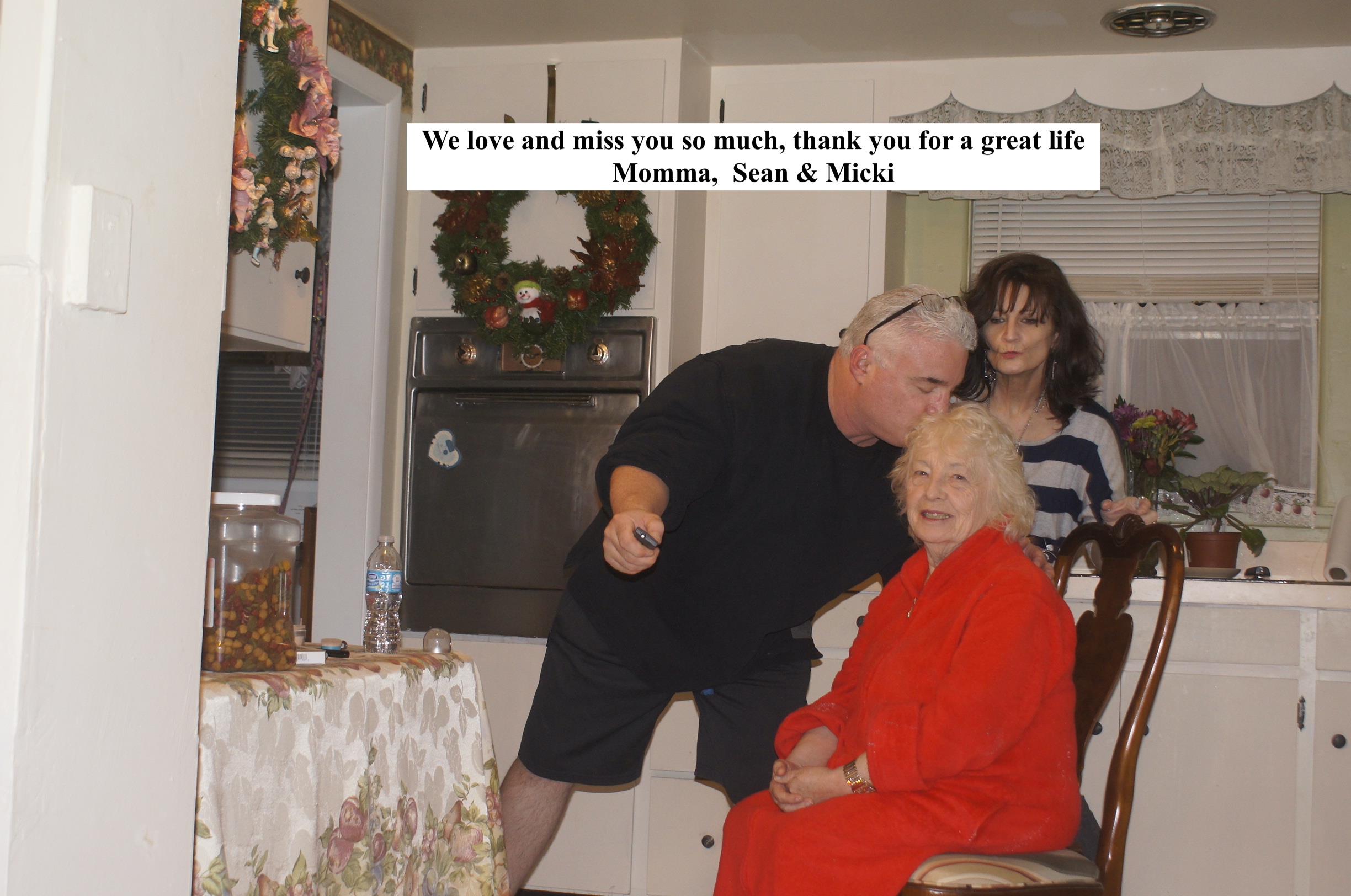 A heartfelt moment in a warm kitchen as family expresses love to a cherished older woman.