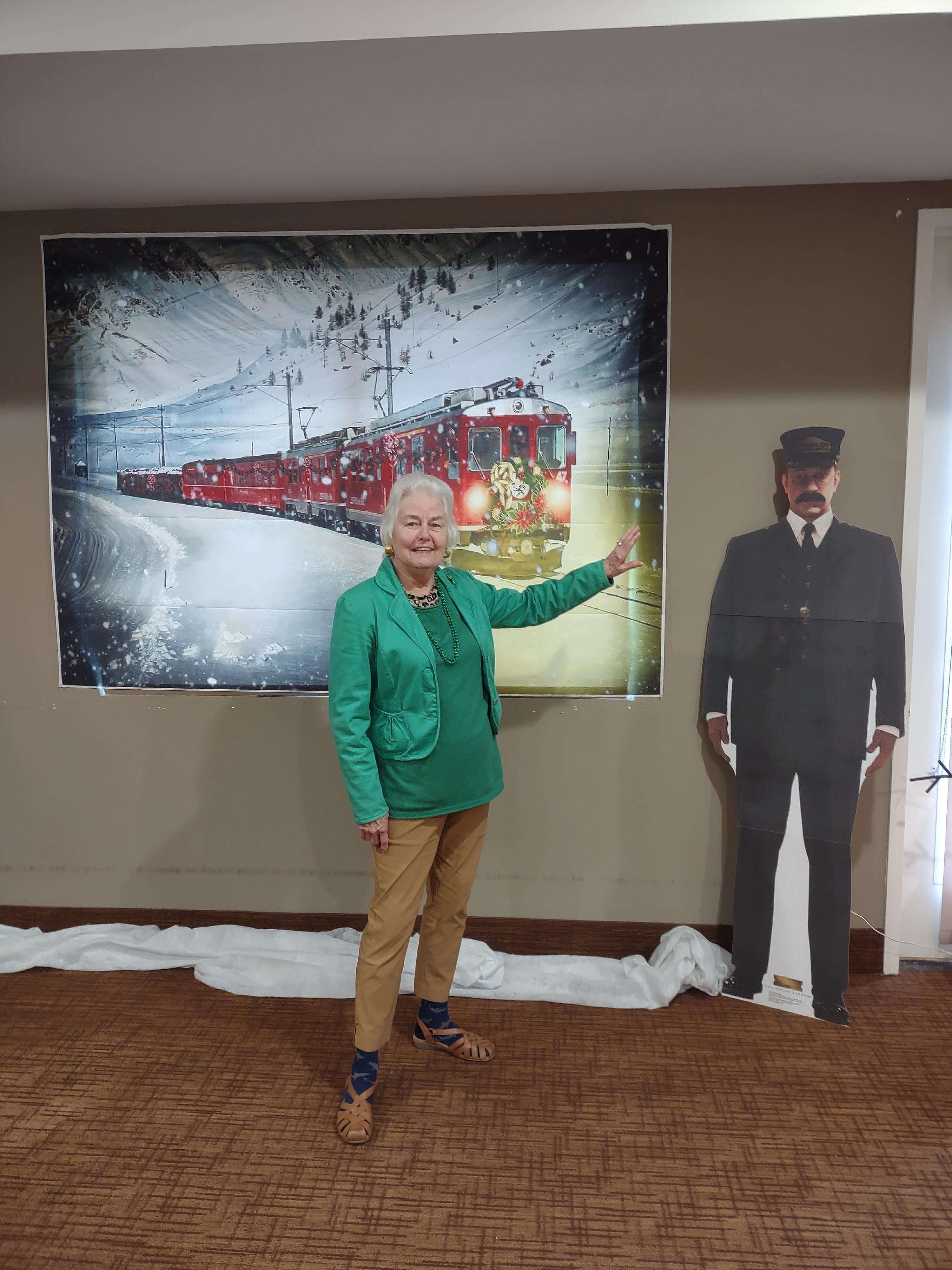 Woman dressed in green stands next to a festive train mural and a cardboard conductor.
