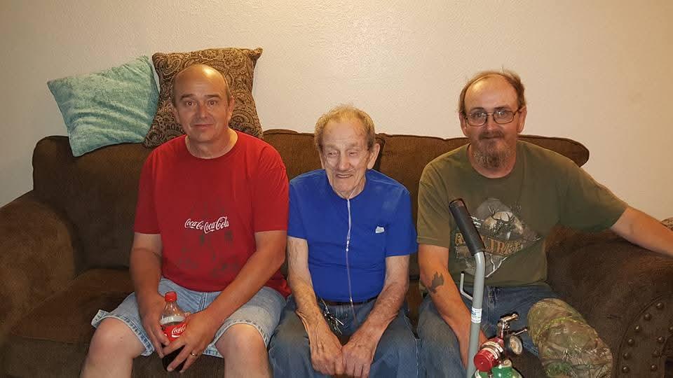 Three men sit closely on a couch, sharing smiles and conversation during a family visit.