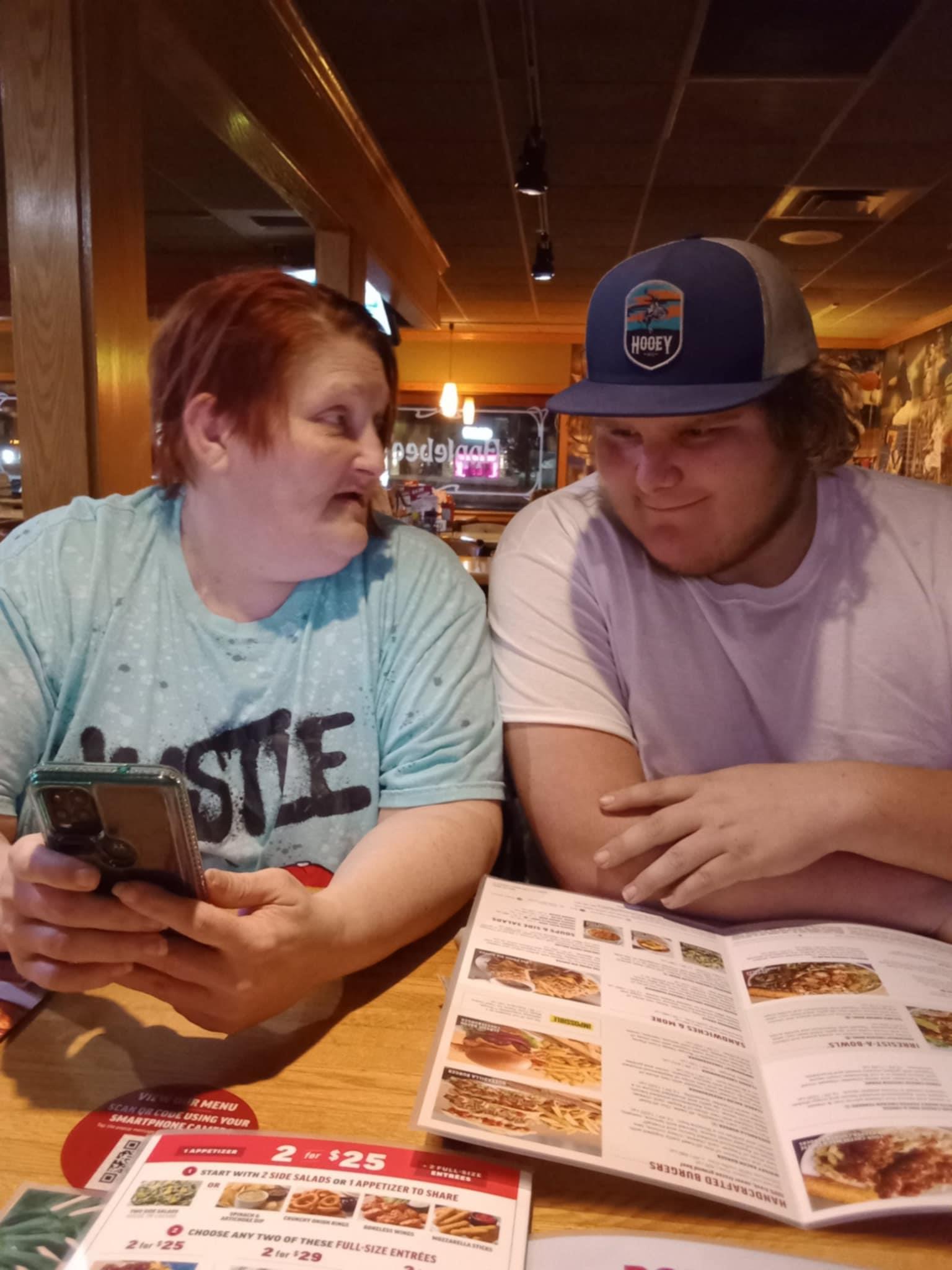 Two friends are seated at a table in a restaurant, looking at each other with smiles.
